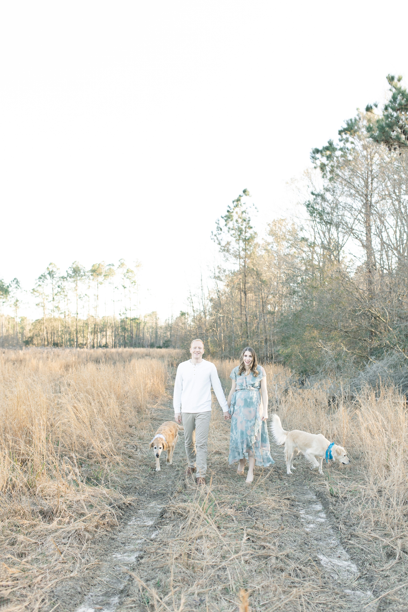 Couple walking through field with two dogs. Photo by Little Sunshine Photography.