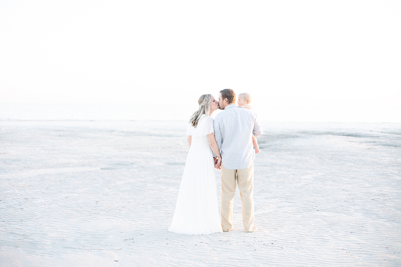 Mom and Dad kissing on the beach at sunset during family photoshoot. Photo by Little Sunshine Photography.