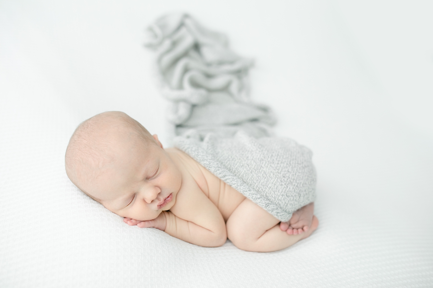 Baby posed with white backdrop and grey knit swaddle by Gulf Shores MS newborn photographer, Little Sunshine Photography.
