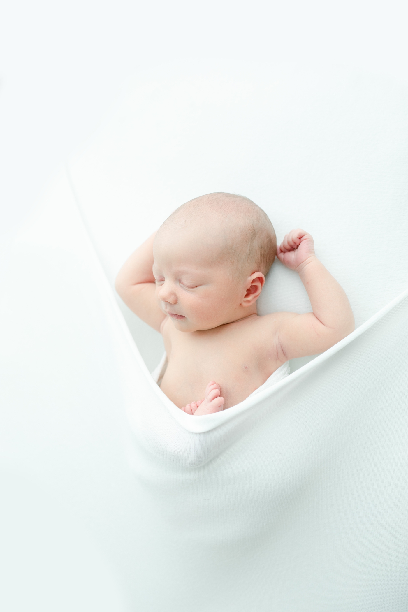 Newborn photoshoot with sleeping baby posed on white backdrop. Photo by Little Sunshine Photography.