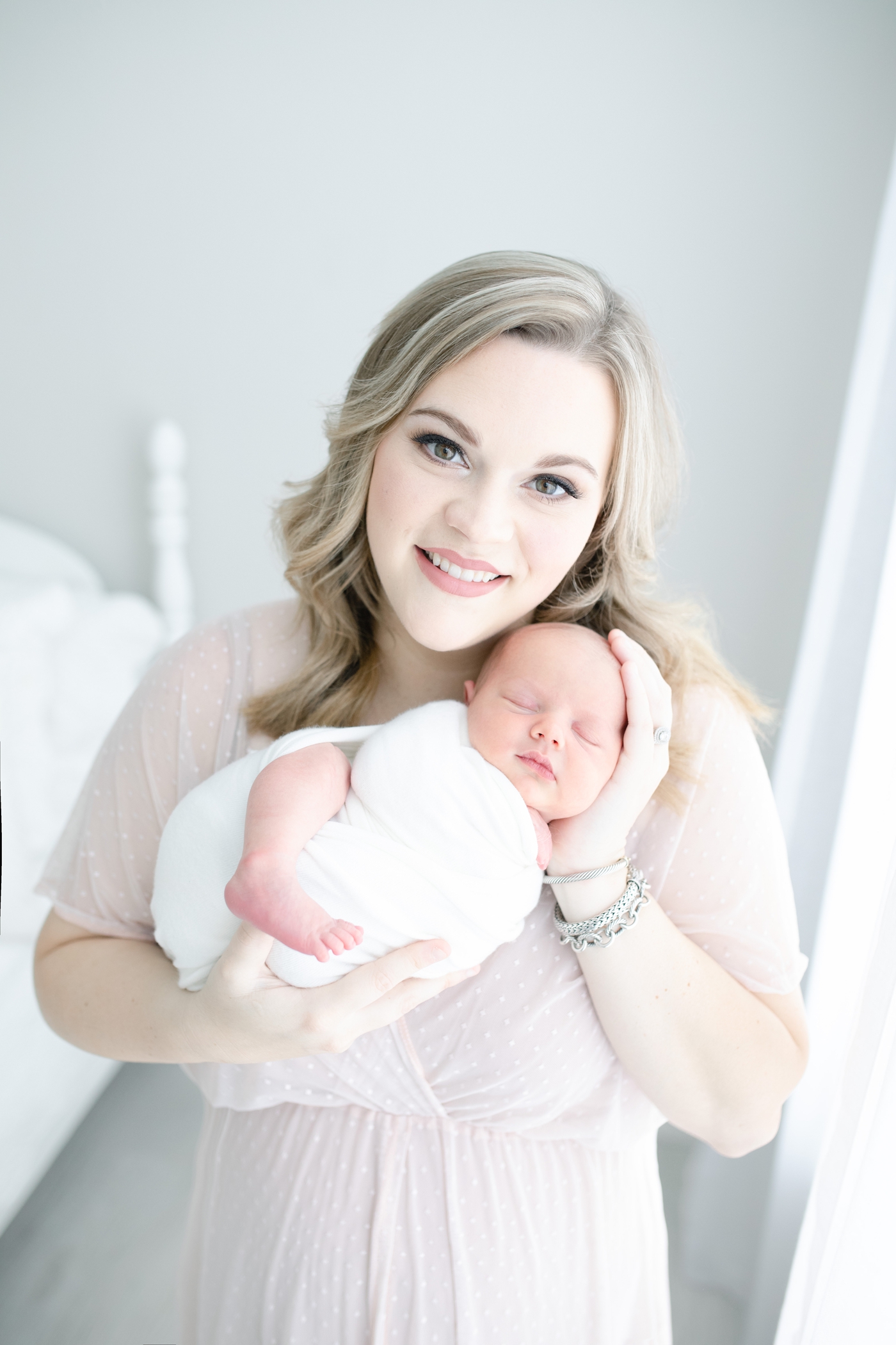 Beautiful Mom holding baby and smiling at camera during newborn photoshoot with Little Sunshine Photography.