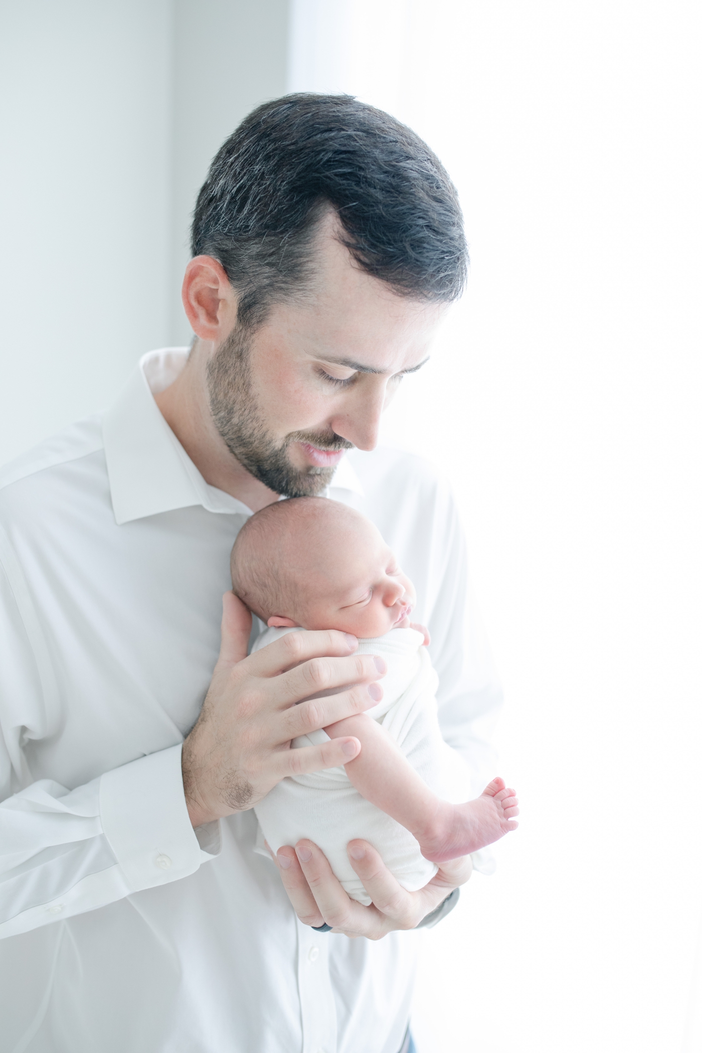 Photo of Dad holding baby near window of studio by Little Sunshine Photography.