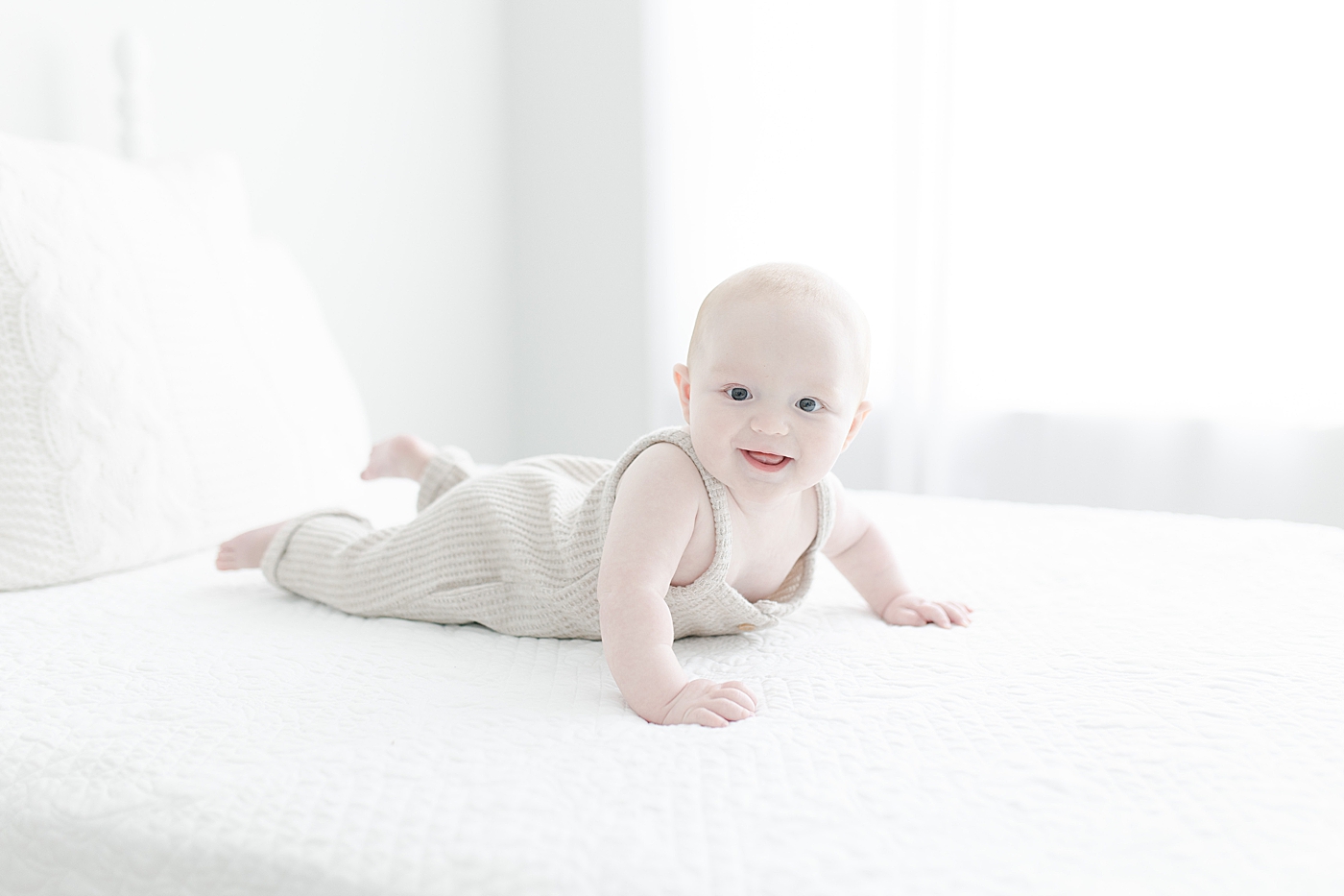 Baby boy wearing knit romper and laying on bed for milestone photoshoot. Photo by Little Sunshine Photography