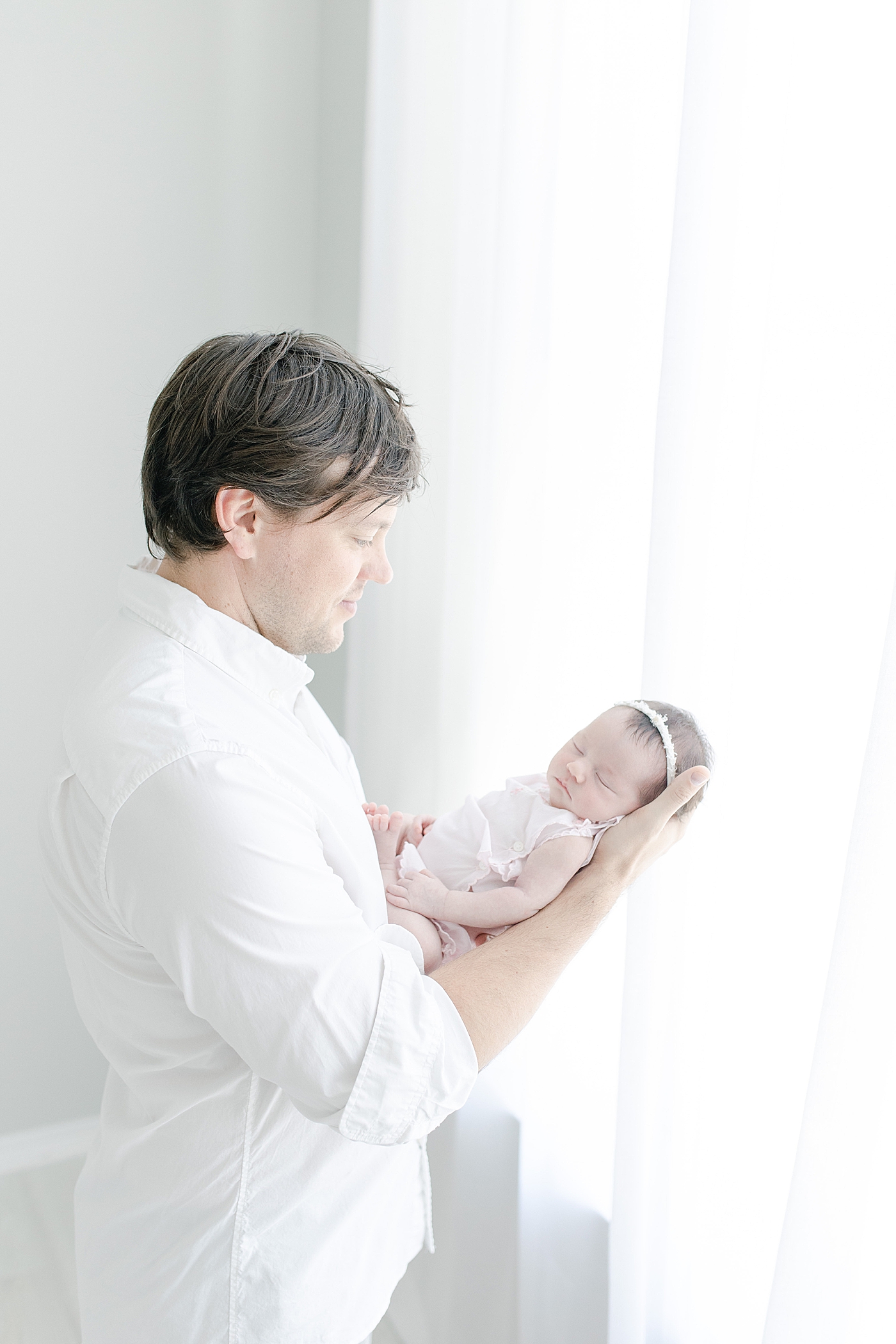 Dad holding his baby girl in front of window. Photo by Little Sunshine Photography