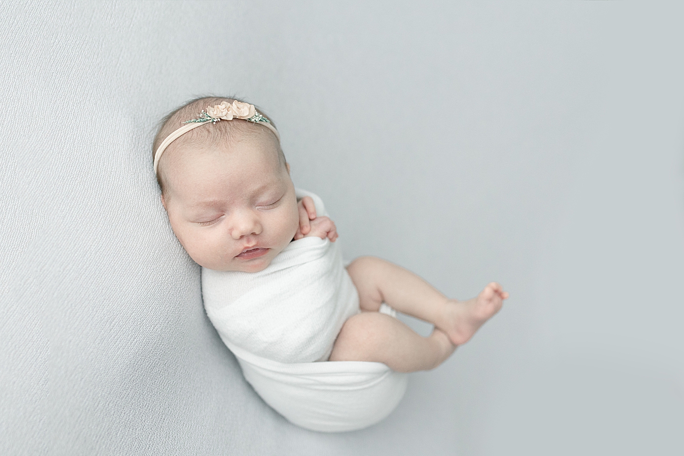 Baby girl wrapped in swaddle with rose headband | Photo by Little Sunshine Photography 
