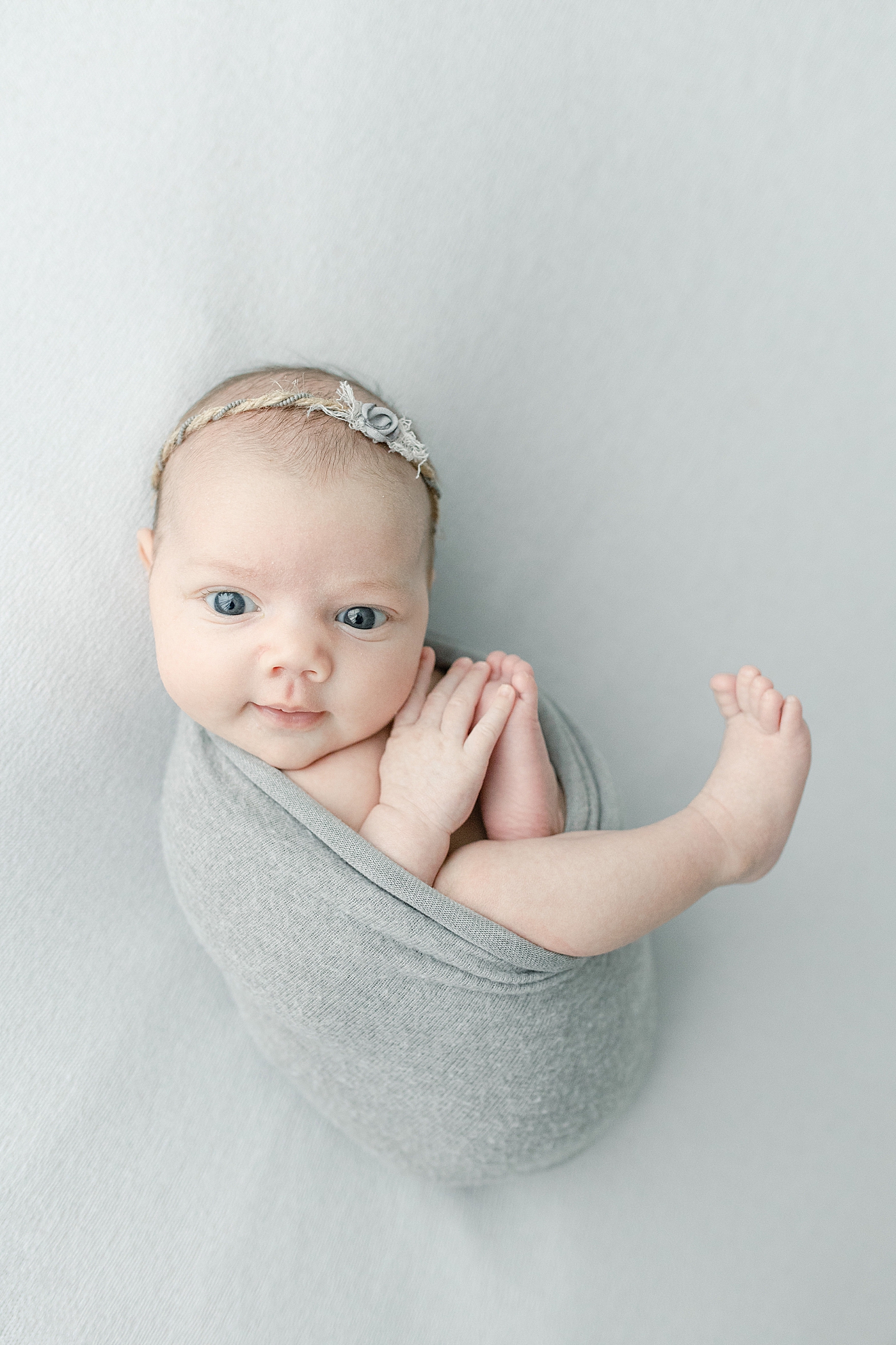 Baby girl in gray swaddle smirking at the camera | Photo by Little Sunshine Photography 