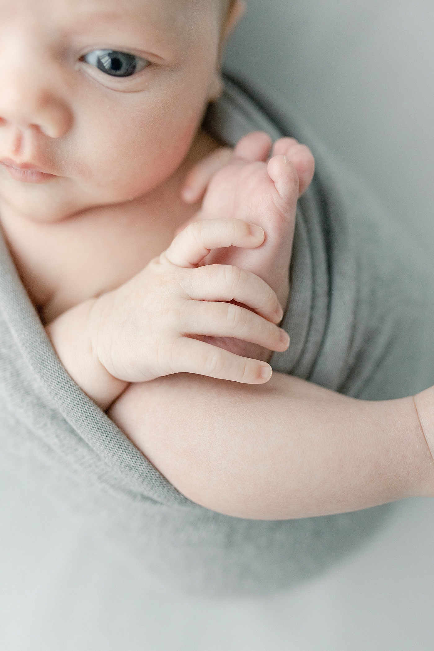 Baby wrapped in gray swaddle details of hands and feet | Photo by Little Sunshine Photography 