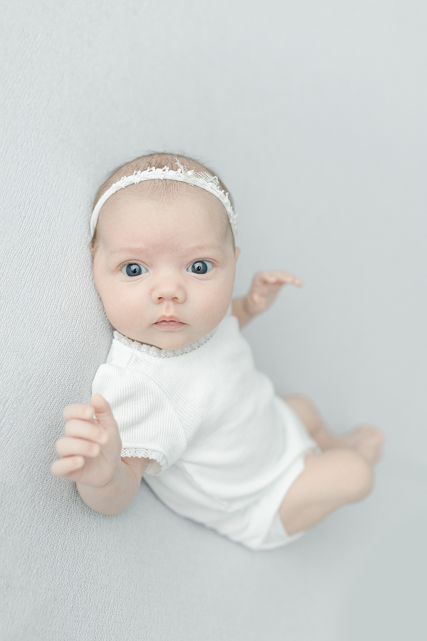 Blue eyed baby girl in white looking at the camera | Photo by Little Sunshine Photography 