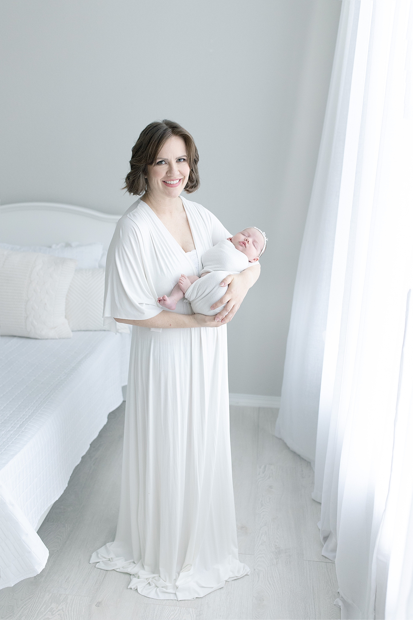 Mom in flowing white dress holding baby girl in a swaddle | Photo by Little Sunshine Photography 