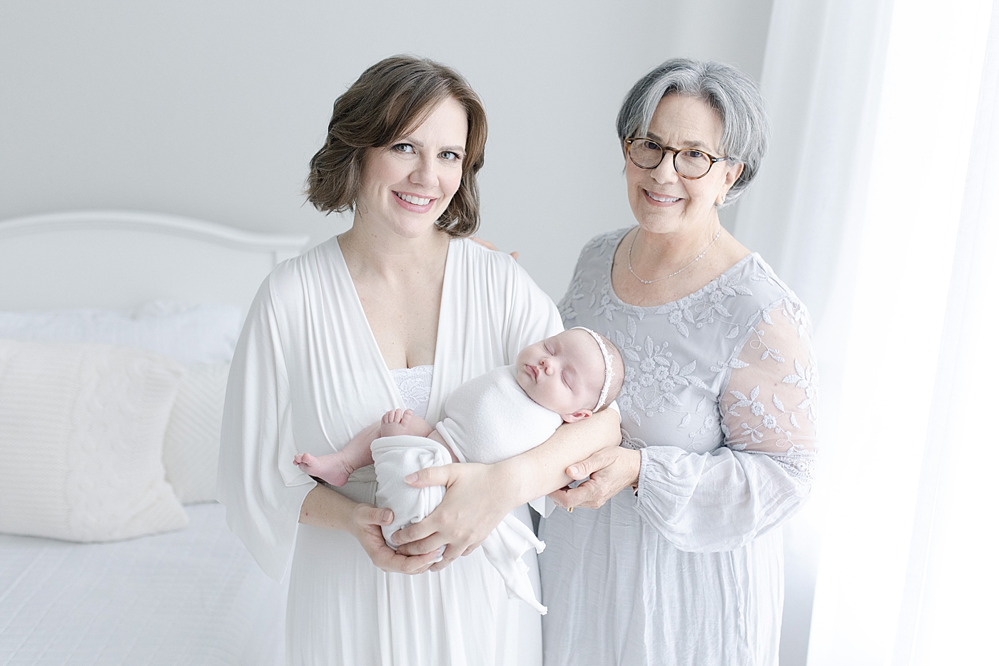 Grandma and mom smile at camera while holding baby girl | Photo with Bay St. Louis newborn photographer Little Sunshine Photography 