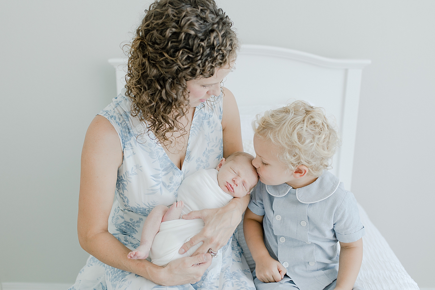 Mom sitting with toddler boy kissing newborn baby's head | Photo by Little Sunshine Photography