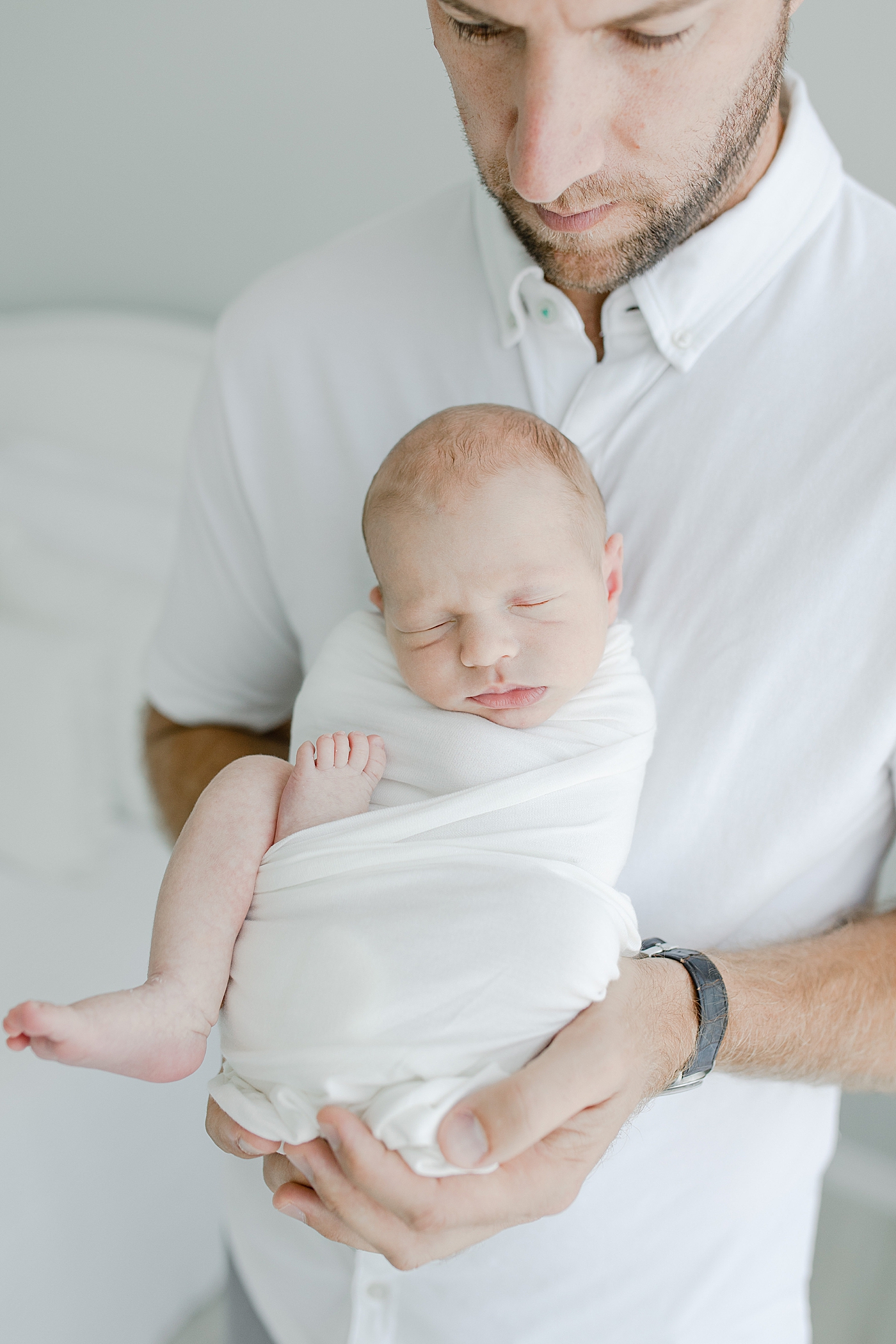 Dad holding newborn baby boy wrapped in white swaddle | Photo by Little Sunshine Photography