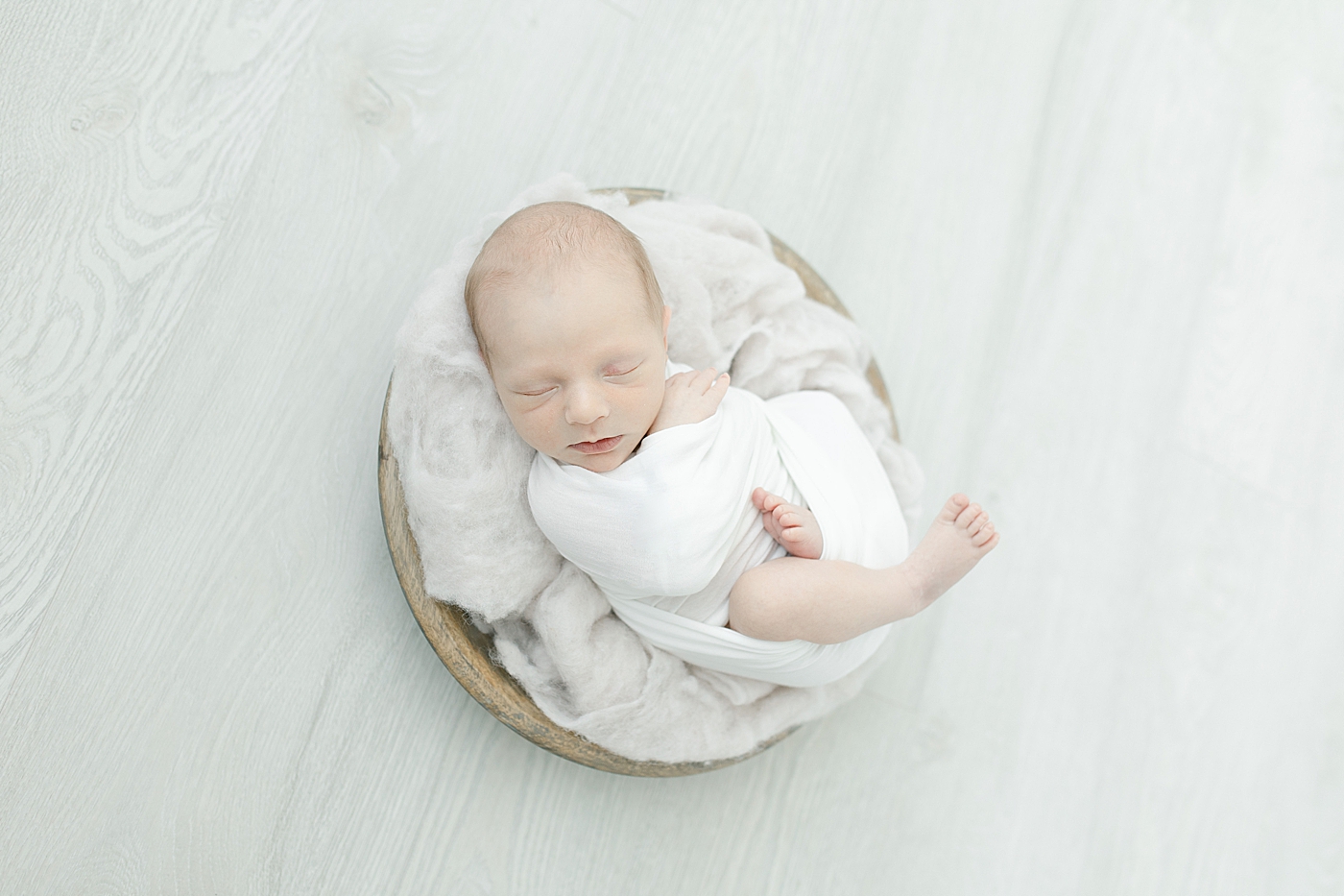 Baby boy in white swaddle in a bowl on white surface | Photo by Little Sunshine Photography