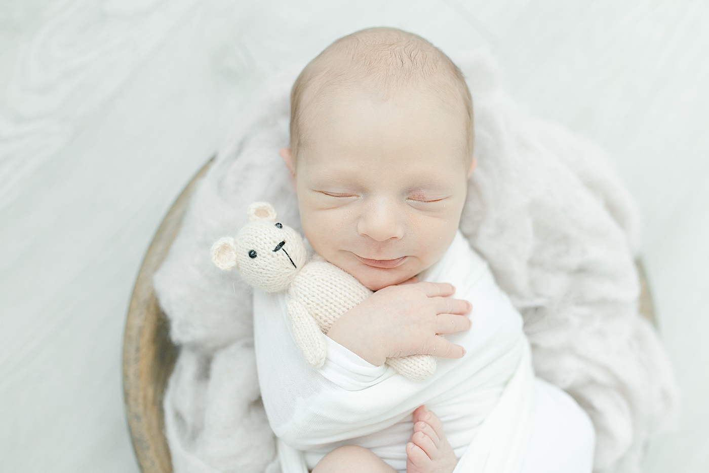 Newborn baby boy in white swaddle snuggling stuffed bear | Photo by Little Sunshine Photography