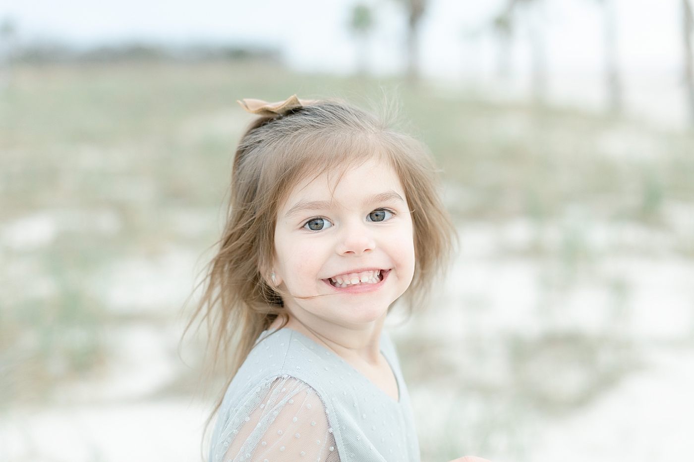 Little girl in blue dress smiling on the beach | Photo by Little Sunshine Photography