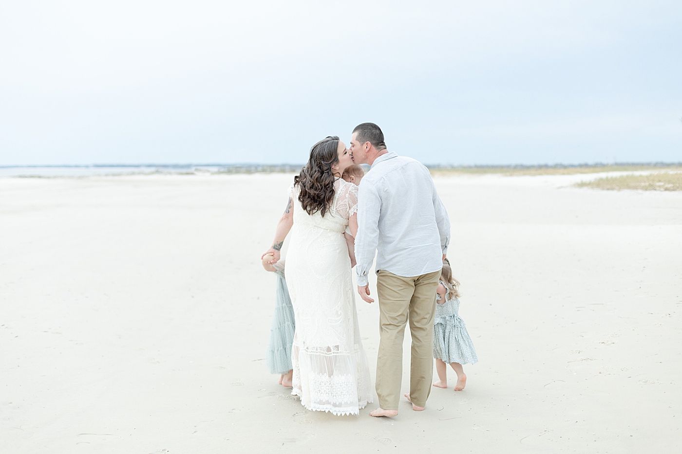 Mom and dad kiss while walking on the beach | Photo by Little Sunshine Photography