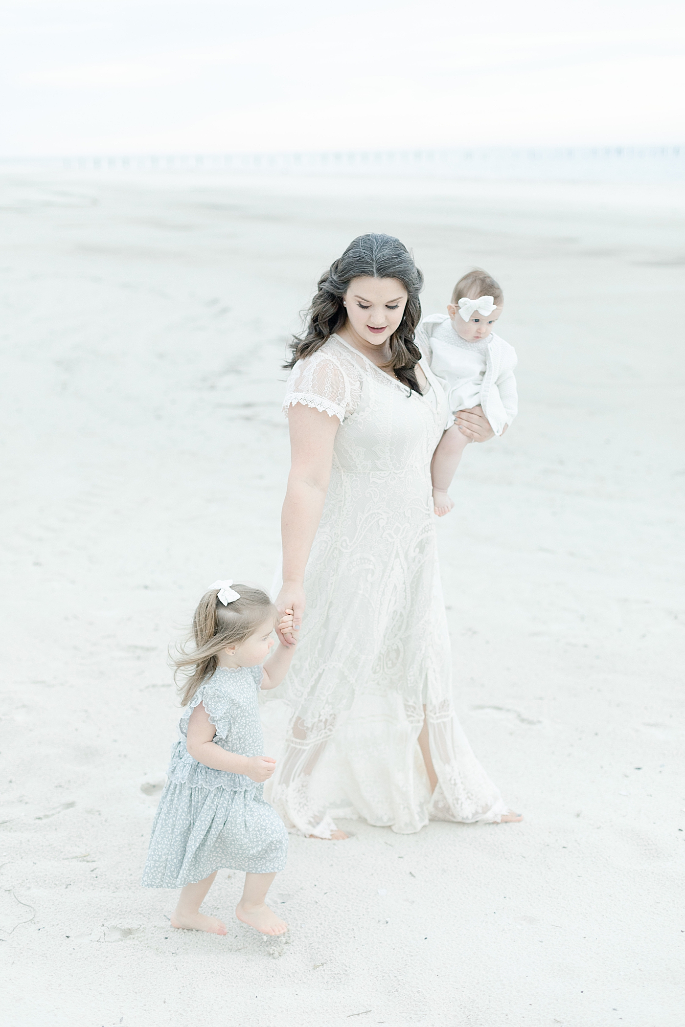 Mom in white holding hands with little girl walking on the beach | Photo by Pascagoula Family Photographer Little Sunshine Photography