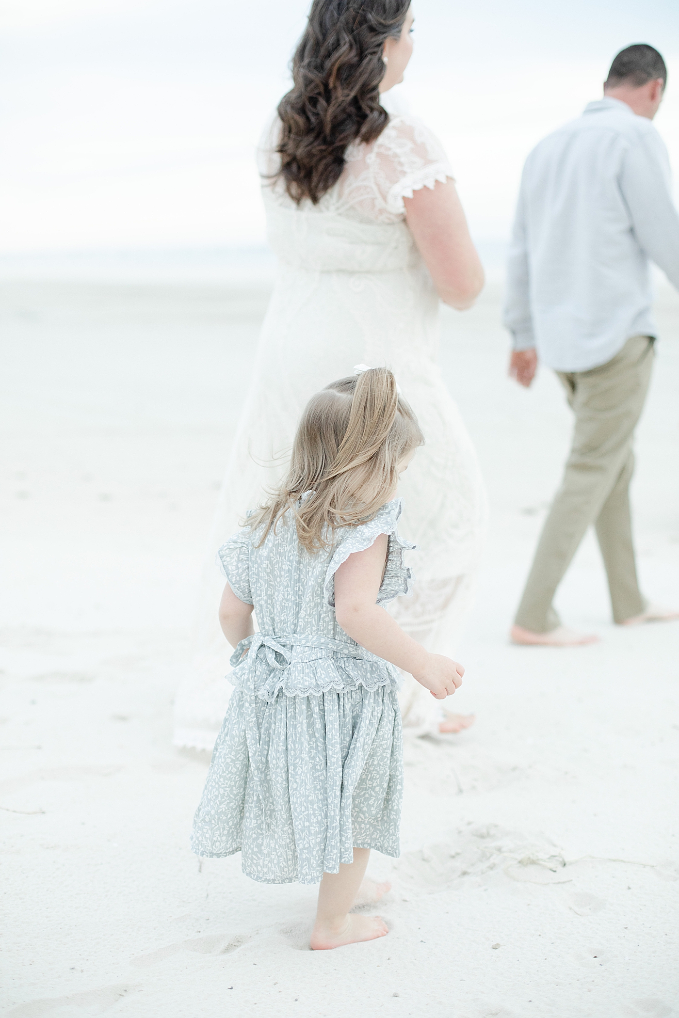 Little girl in blue dress walking behind mom on the beach | Photo by Pascagoula Family Photographer Little Sunshine Photography