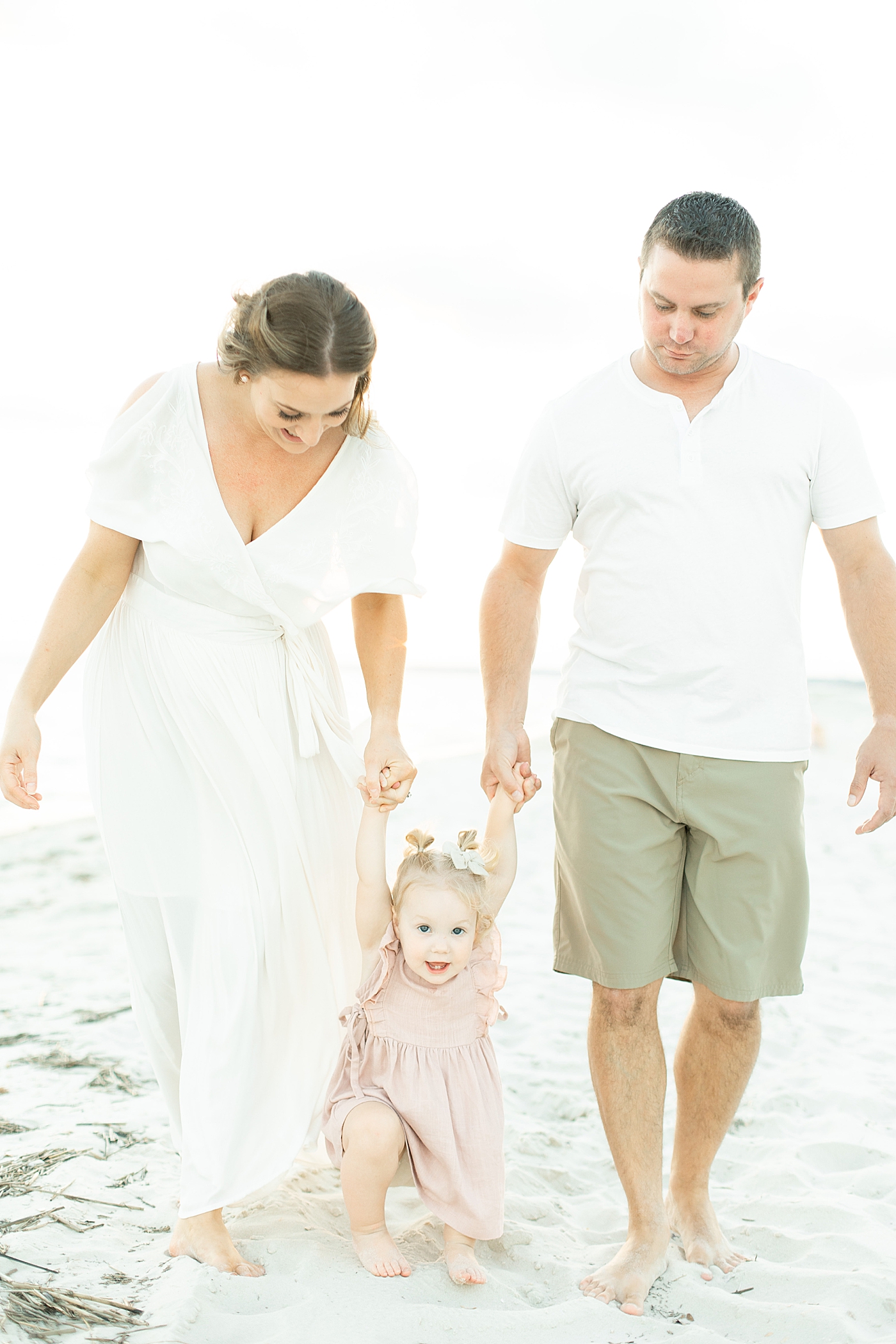 Dad and mom walking with toddler girl in pink dress on the beach | Photo by Little Sunshine Photography