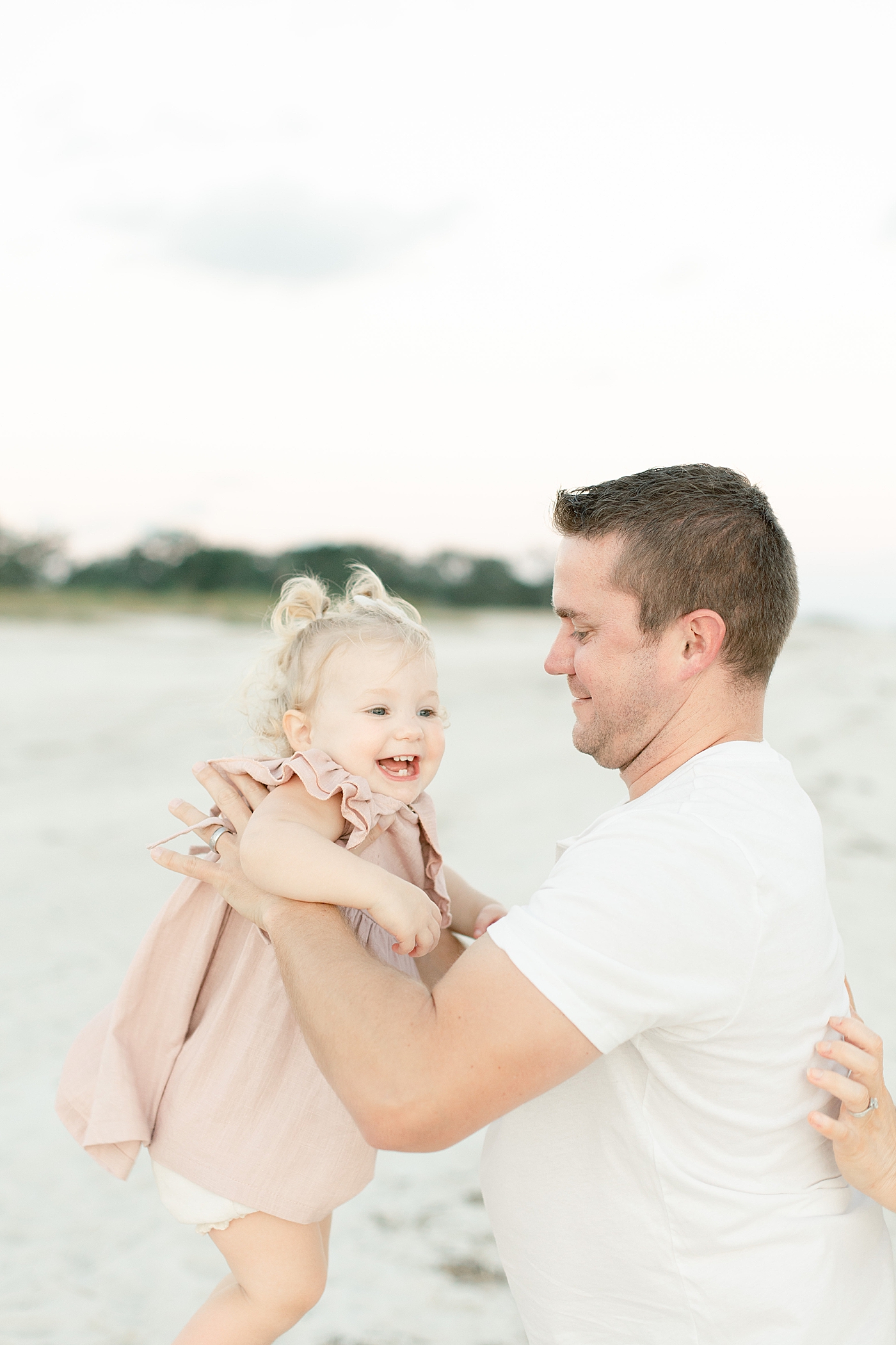 Dad holding toddler baby in a pink dress on the beach | Photo by Little Sunshine Photography