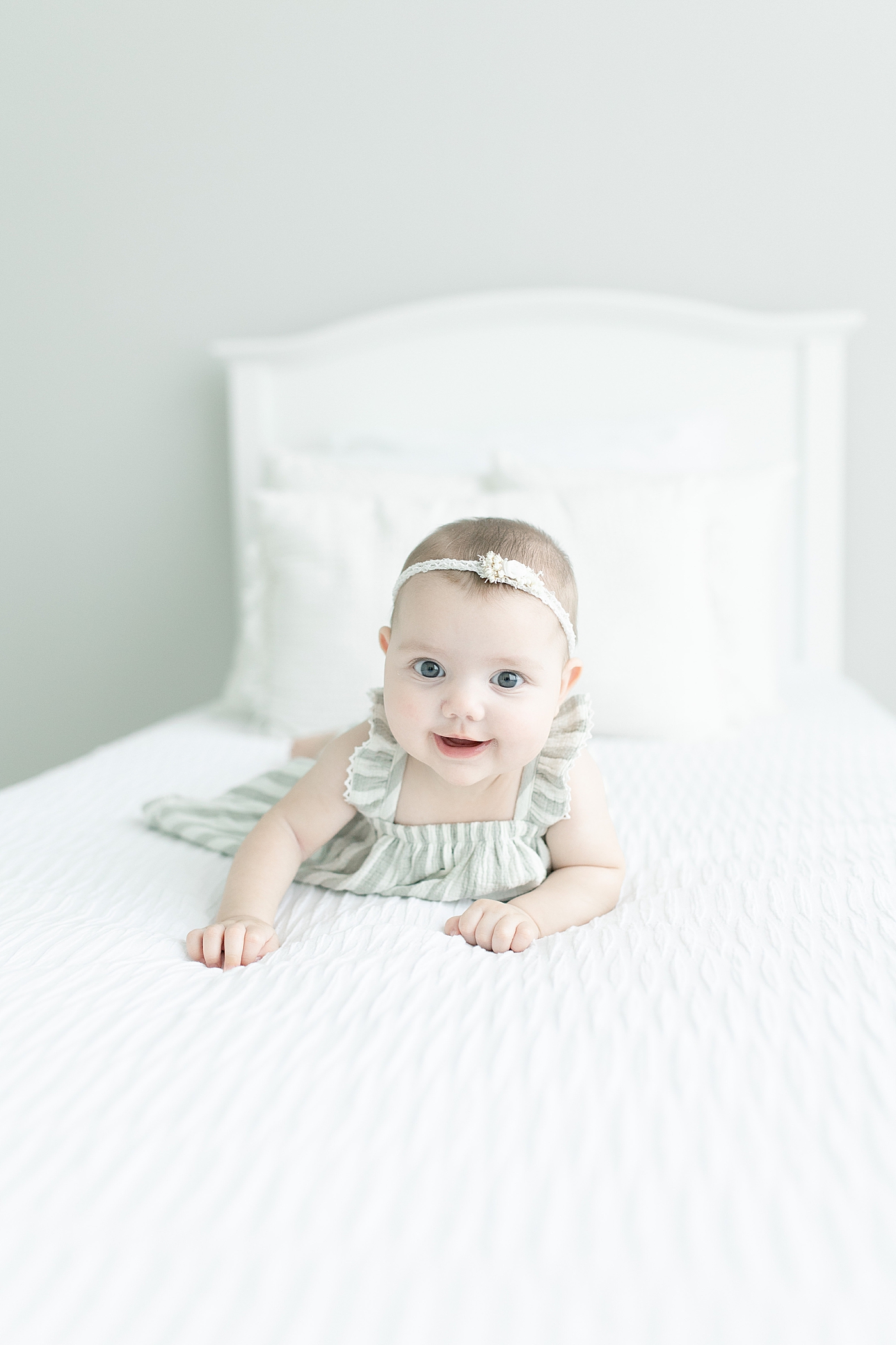Baby girl in stripes smiling while laying on her belly | Photo by Little Sunshine Photography