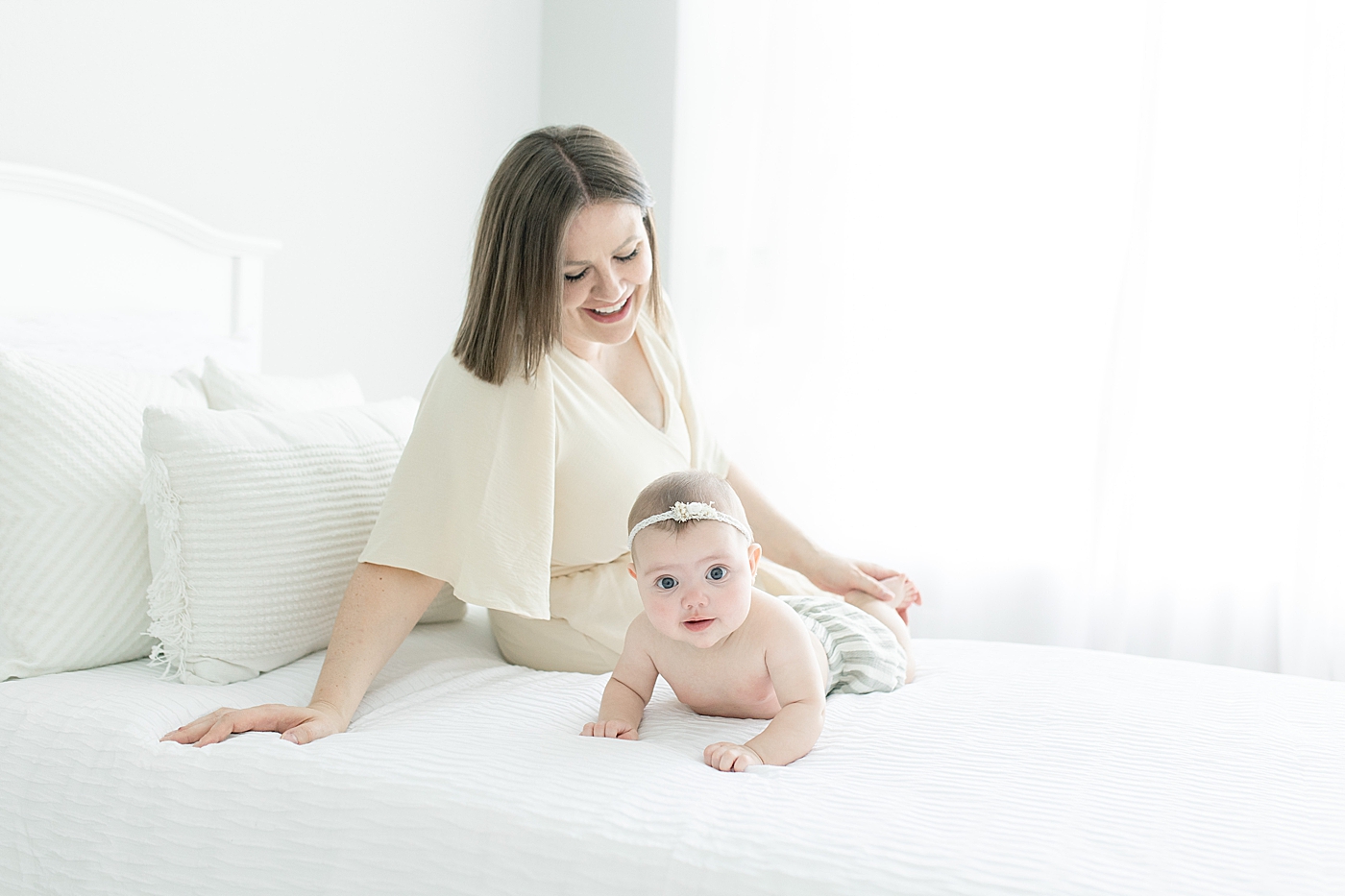 Baby girl and mom sitting on a bed during tummy time | Photo by Little Sunshine Photography