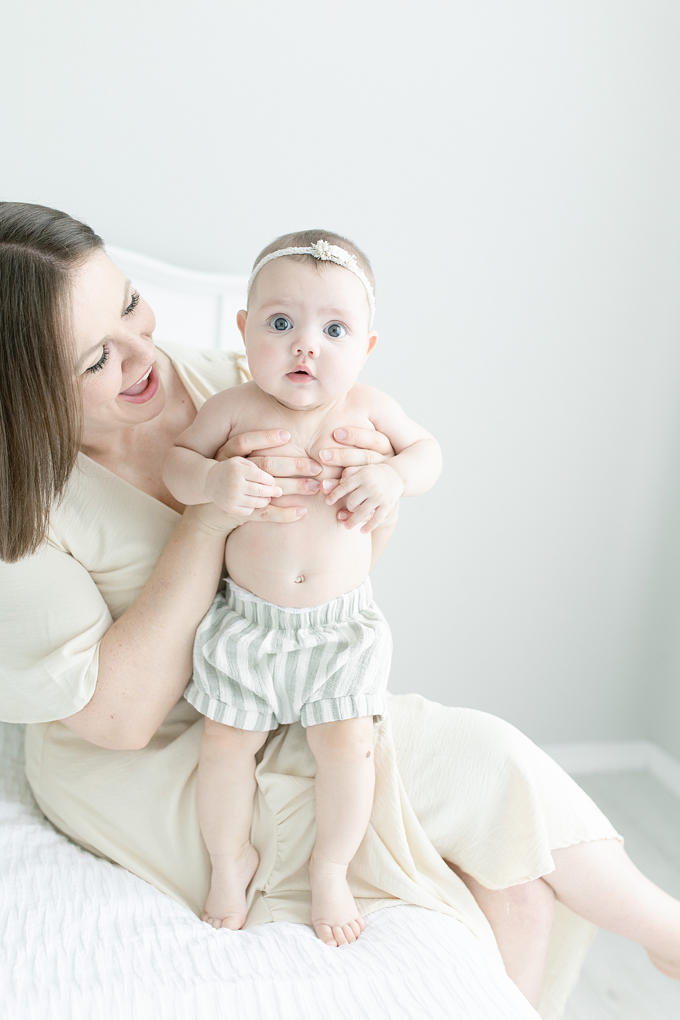 Smiling mom helping baby girl in bloomers stand | Photo by Little Sunshine Photography