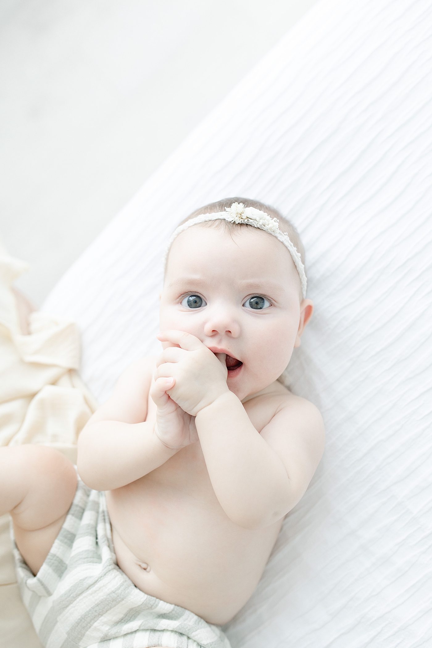 Baby girl in striped chewing on her thumb | Photo by Little Sunshine Photography