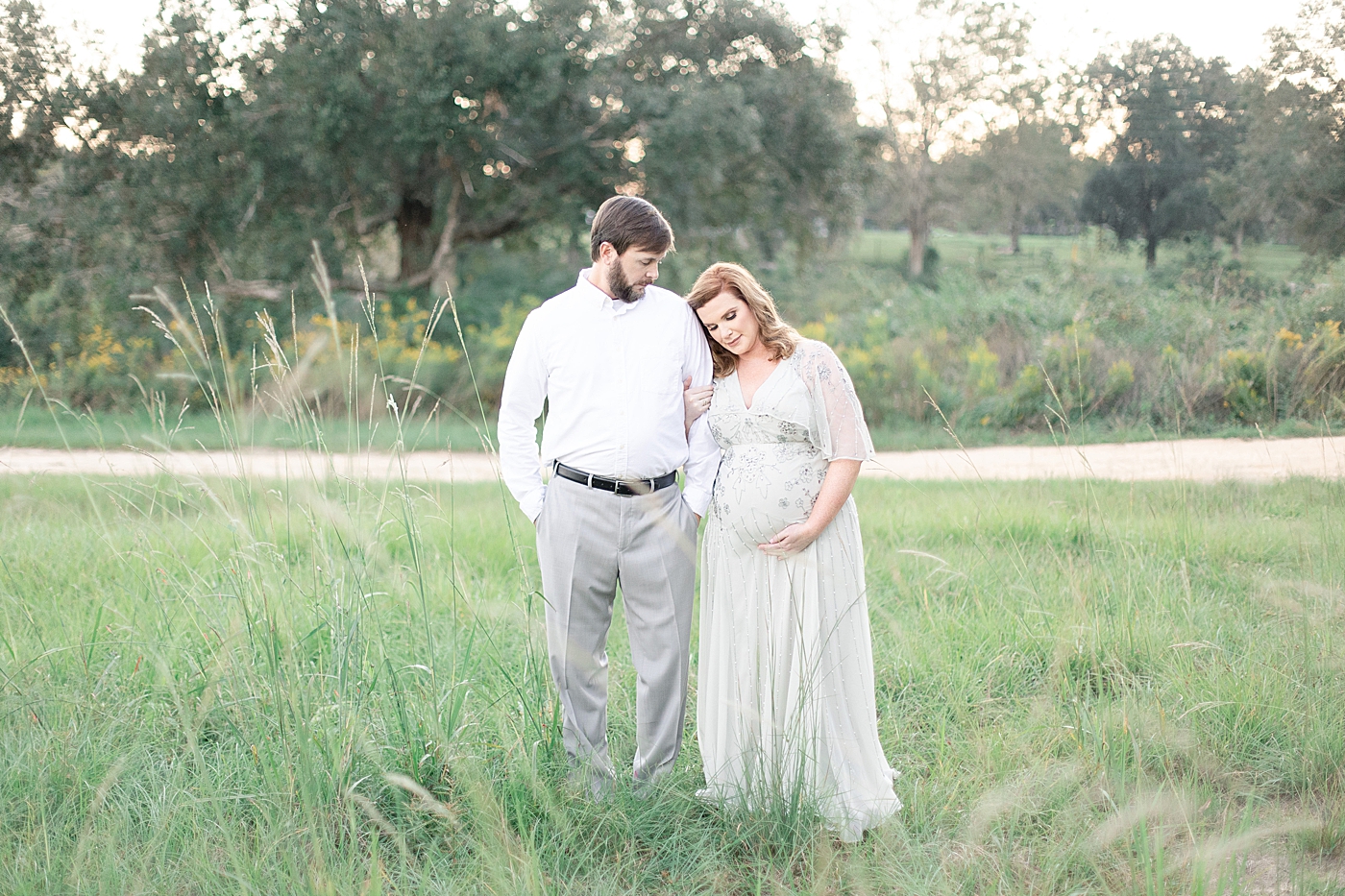 Mother to be and father to be standing in a field | Photo by Little Sunshine Photography