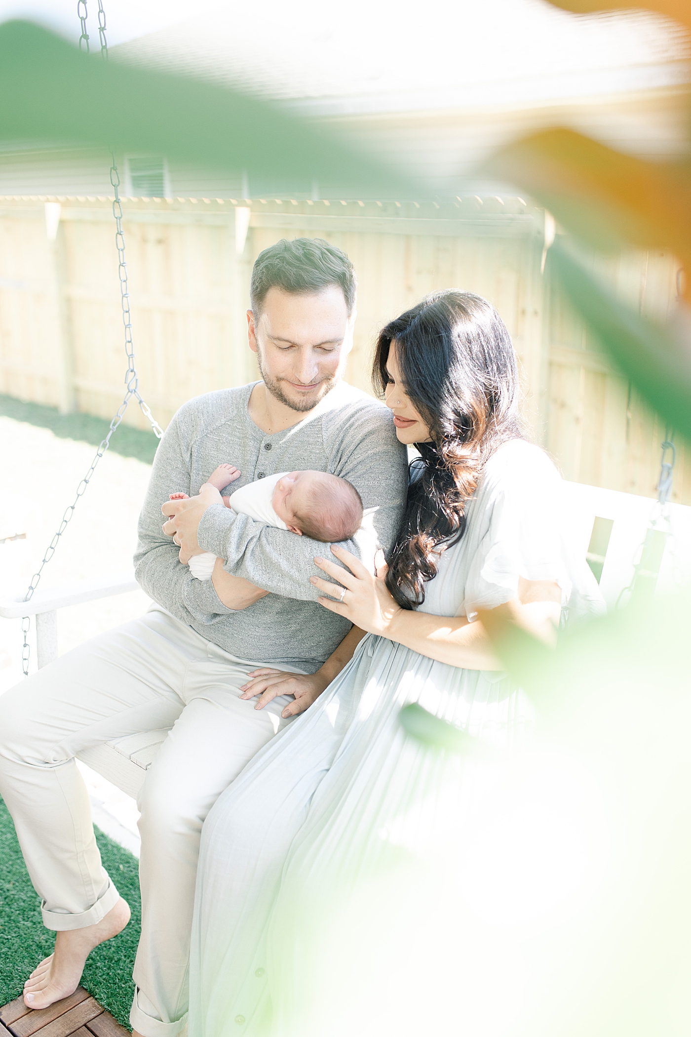 Mom dad and newborn baby sitting on porch swing | Photo by Little Sunshine Photography