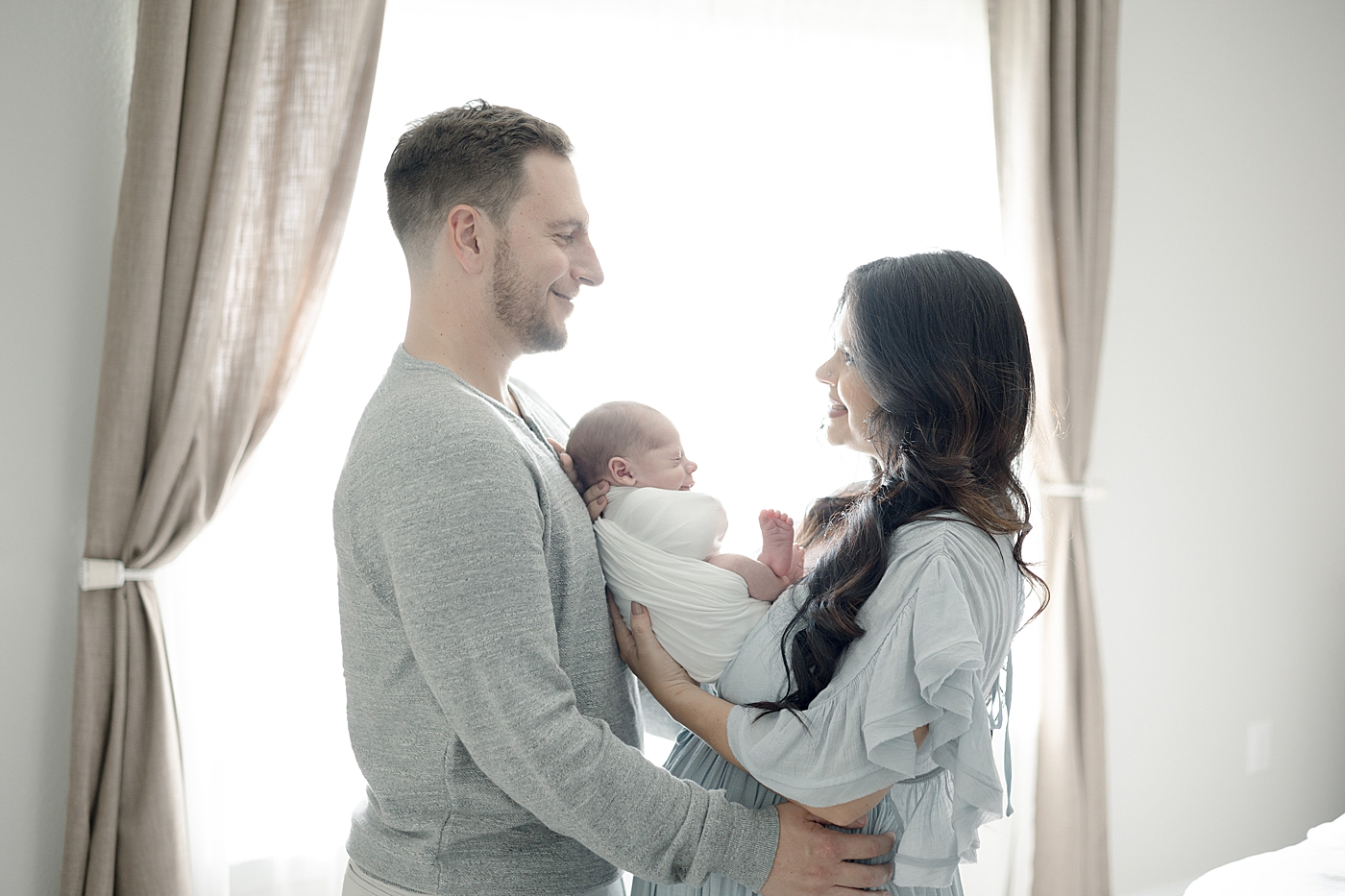 Mom and dad holding newborn baby together in their home | Photo by Little Sunshine Photography
