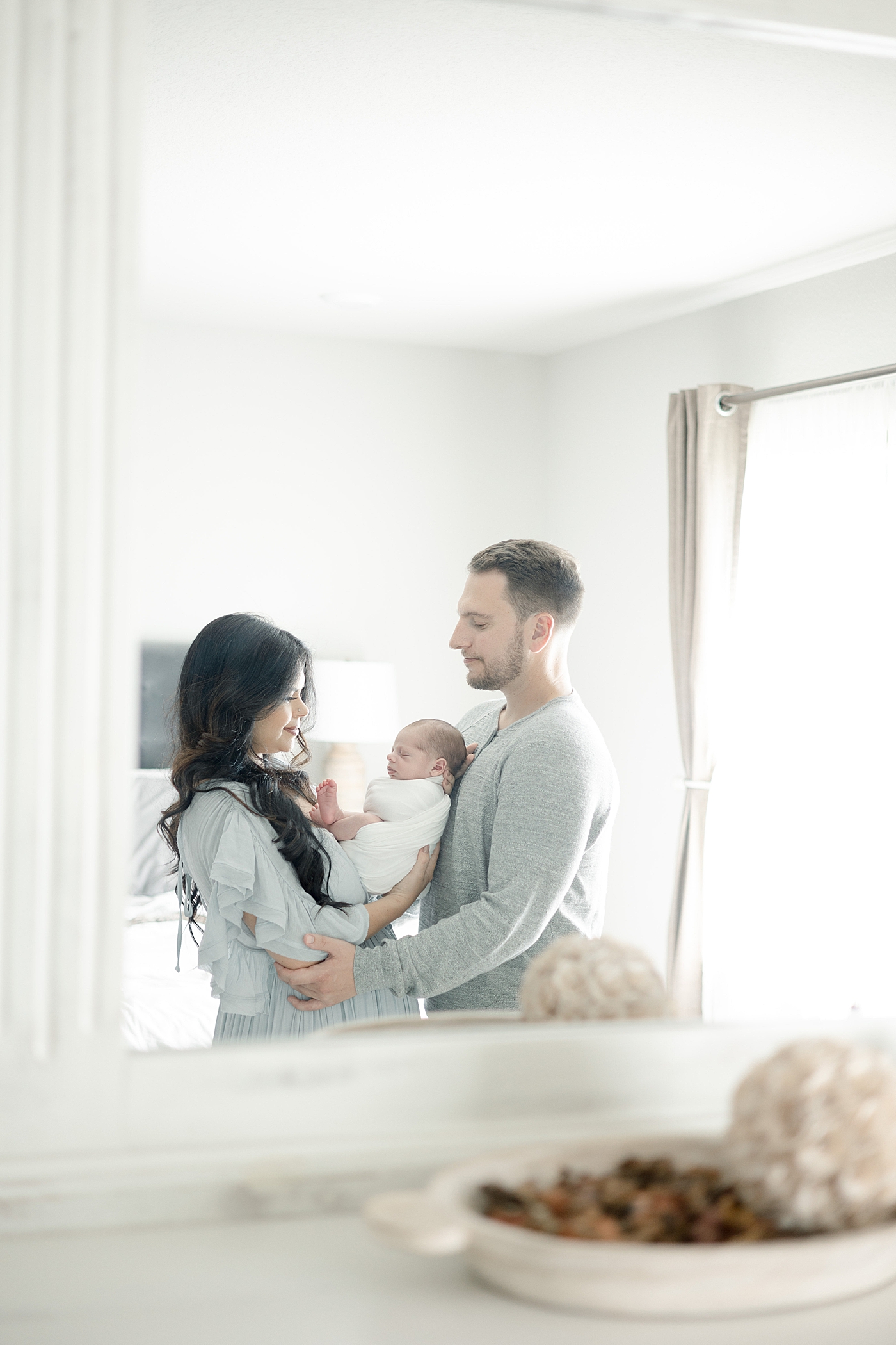 Mom and dad holding new baby in mirror reflection | Photo by Biloxi MS newborn photographer Little Sunshine Photography