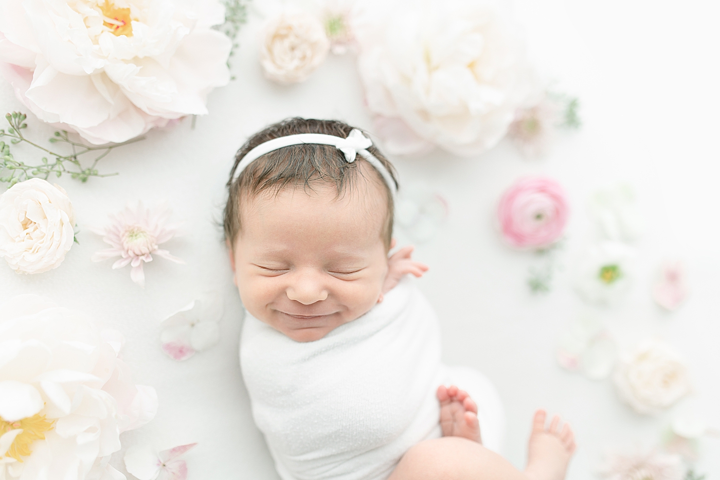 Smiling newborn baby girl surrounded by flowers | Photo by Little Sunshine Photography 