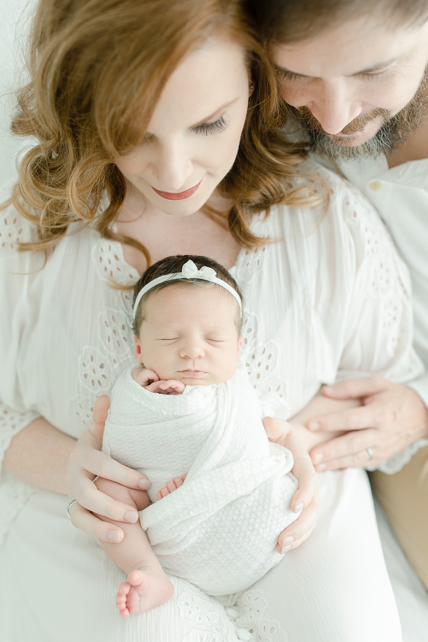 Sleeping newborn baby girl in white swaddle held by parents | Photo by Little Sunshine Photography 