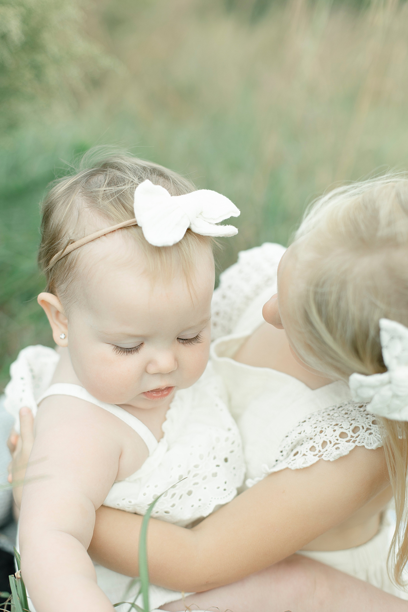 Sisters in white snuggling together in a field | Photo by Little Sunshine Photography 