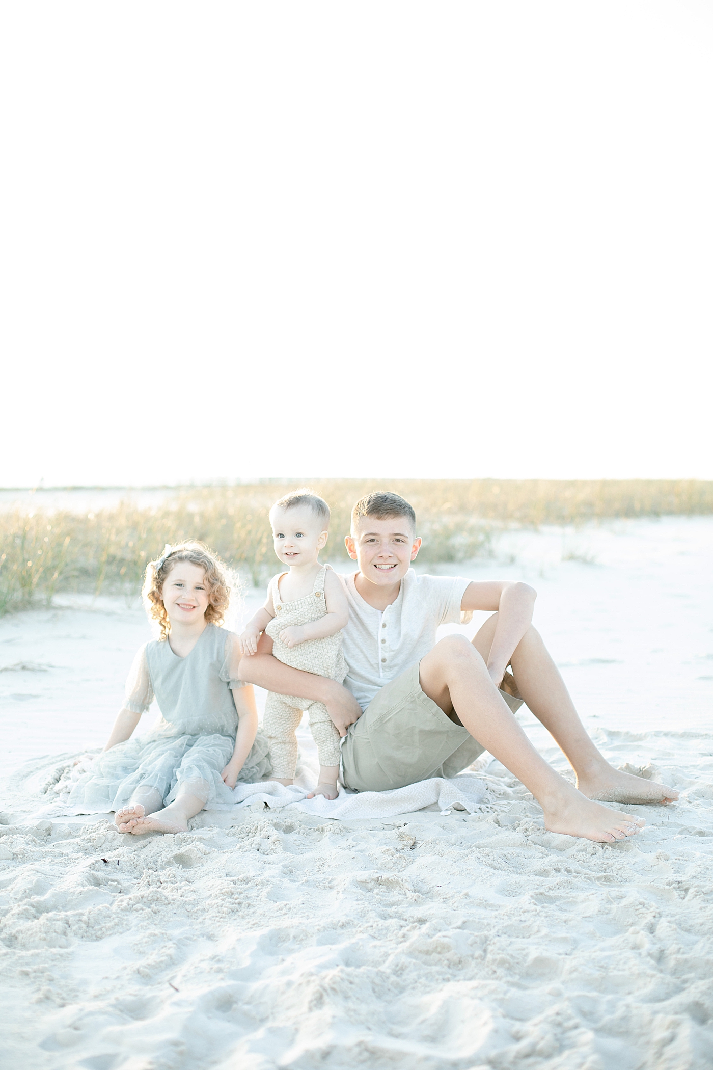 Three kids sitting on the beach together | Photo by Ocean Springs Family Photographer Little Sunshine Photography