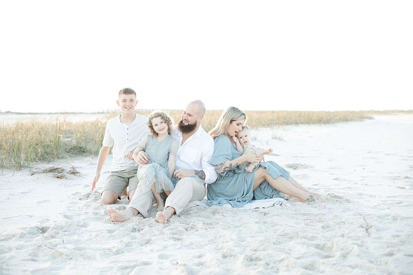 Family of four sitting on the beach together | Photo by Little Sunshine Photography