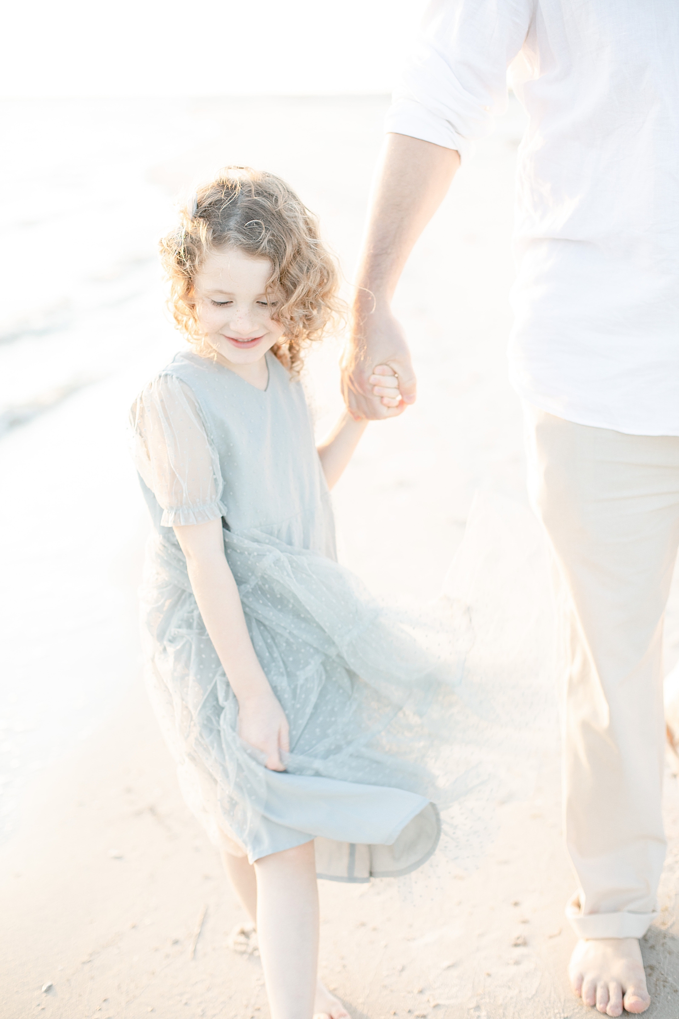 Little girl holding dads hand on the beach | Photo by Ocean Springs Family Photographer Little Sunshine Photography