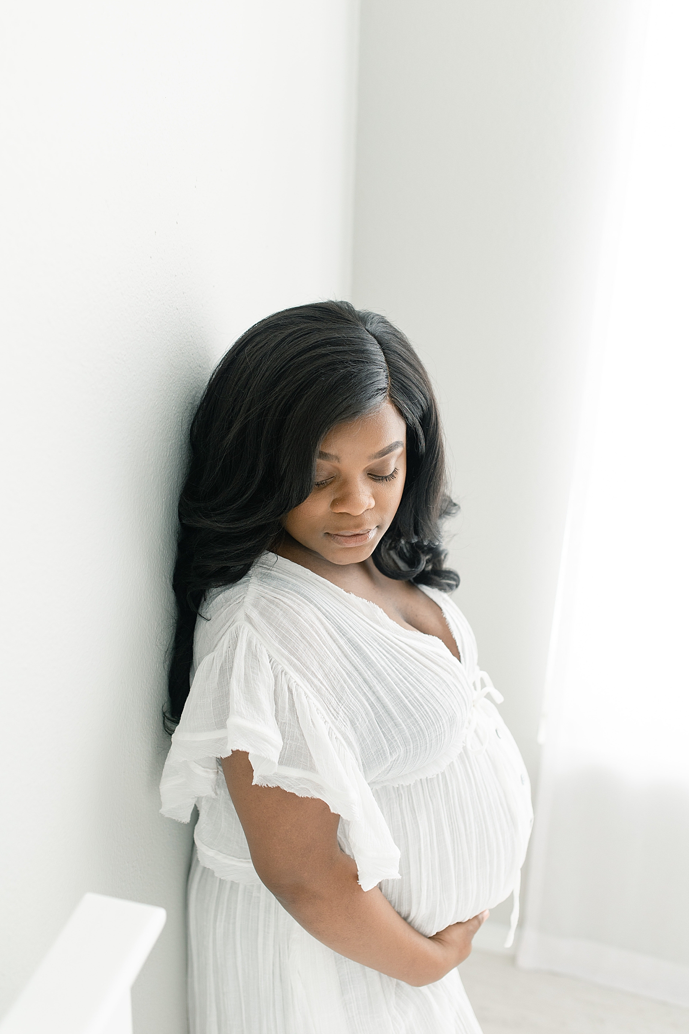 Mother to be in white dress looking down at her belly | Photo by Little Sunshine Photography