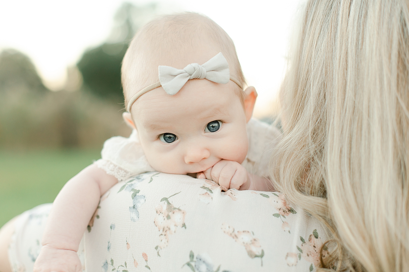 Baby girl with a bow held by mom | Photo by Little Sunshine Photography