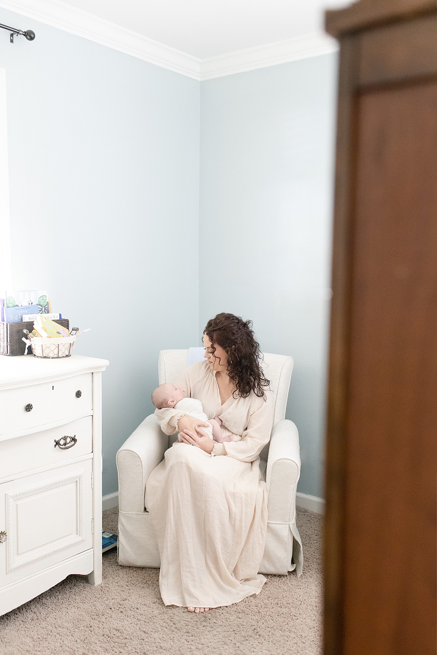 Mom in cream dress rocking her new baby in the nursery | Photo by Little Sunshine Photography