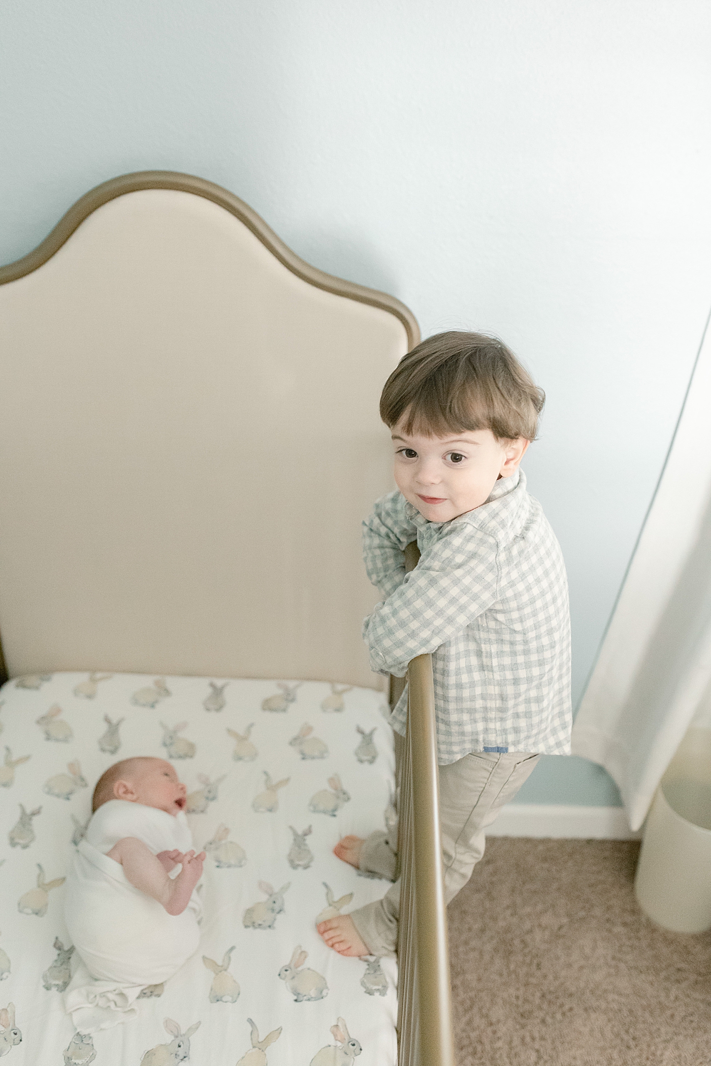 Toddler brother standing on side of crib to look at new baby | Photo by Little Sunshine Photography