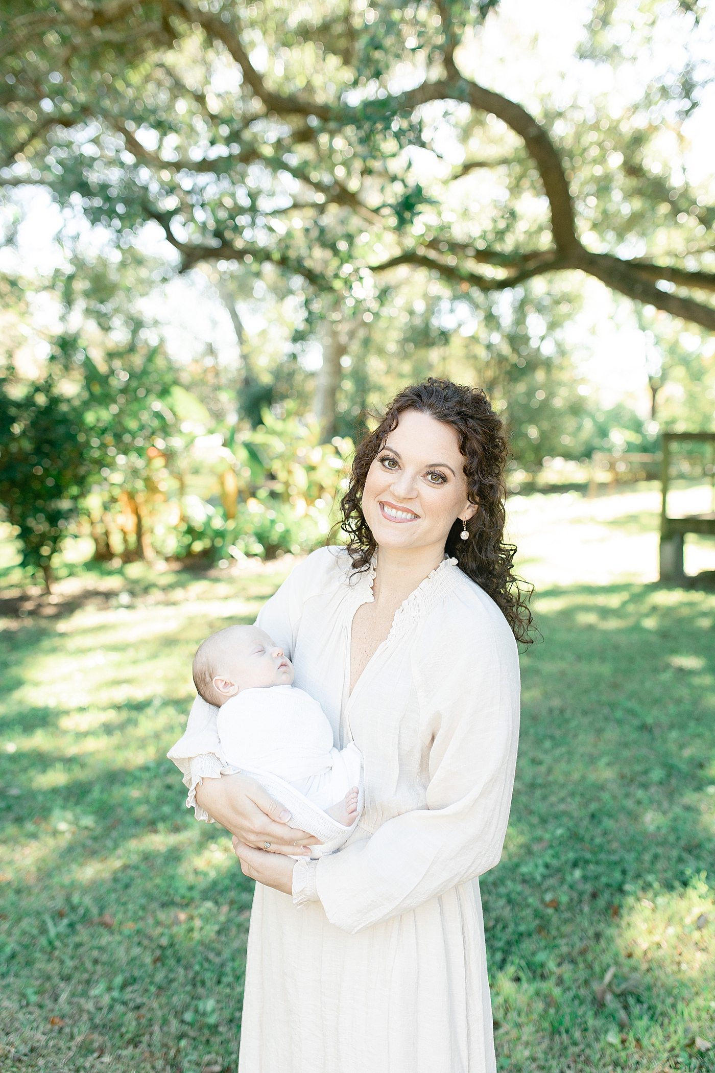 Mom in cream dress smiling holding her new baby | Photo by Little Sunshine Photography