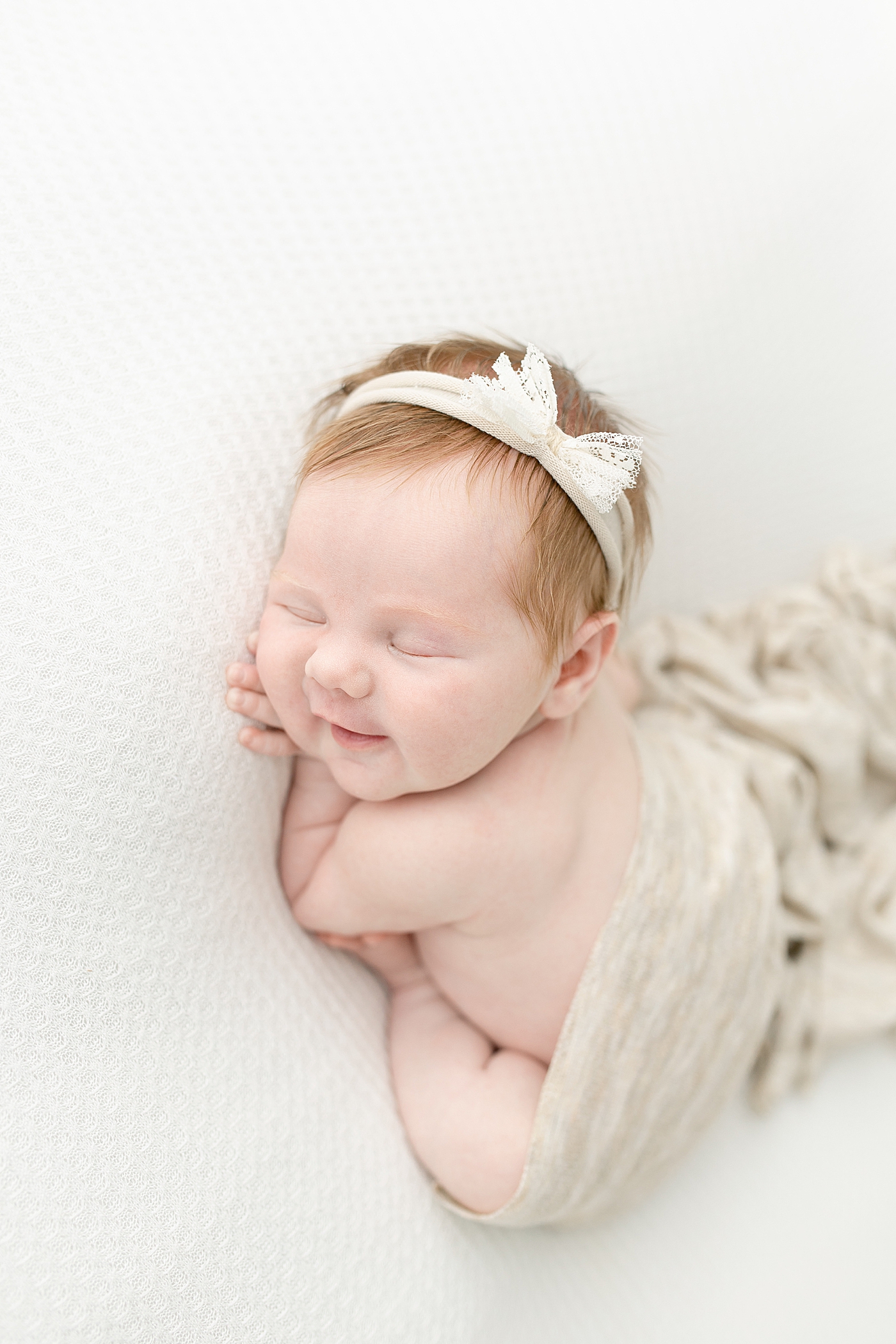 Newborn baby girl smiling wrapped in gray swaddle | Photo by Little Sunshine Photography