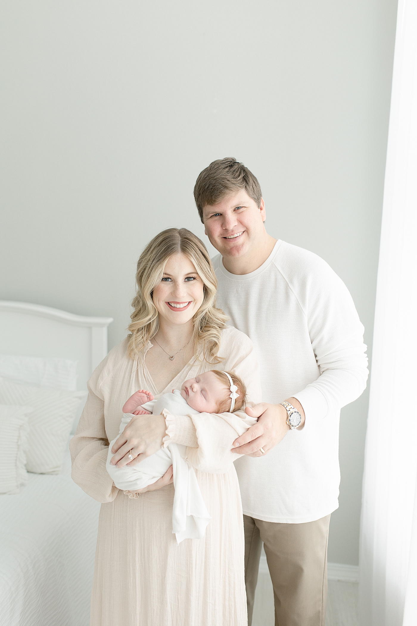Mom and dad smiling holding their newborn baby girl | Photo by Little Sunshine Photography