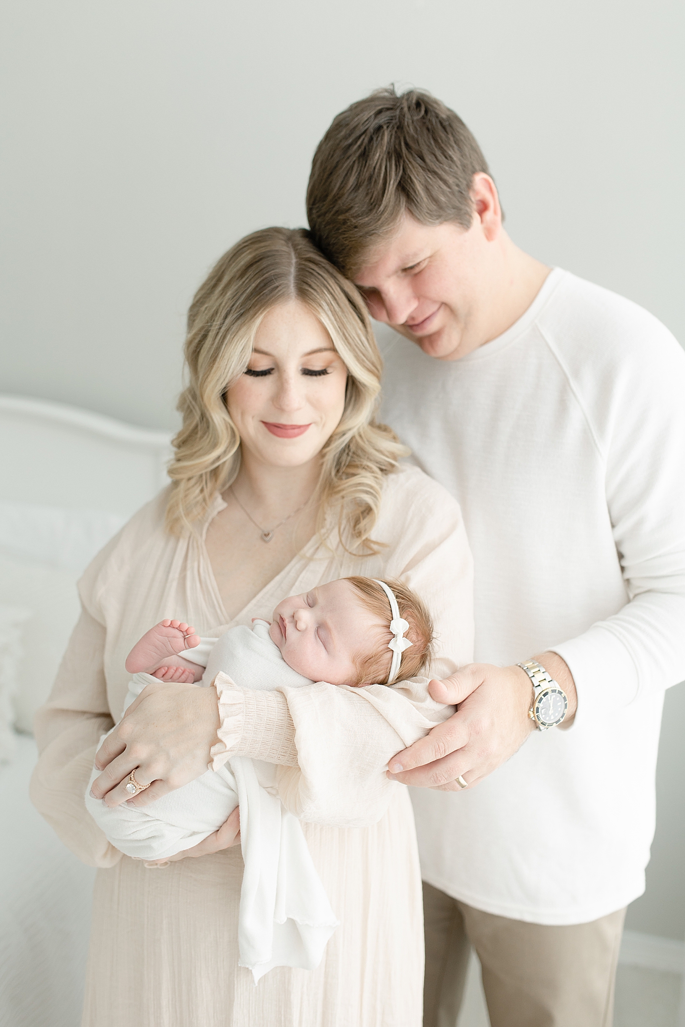 Mom and dad in neutrals holding their newborn baby girl | Photo by Little Sunshine Photography