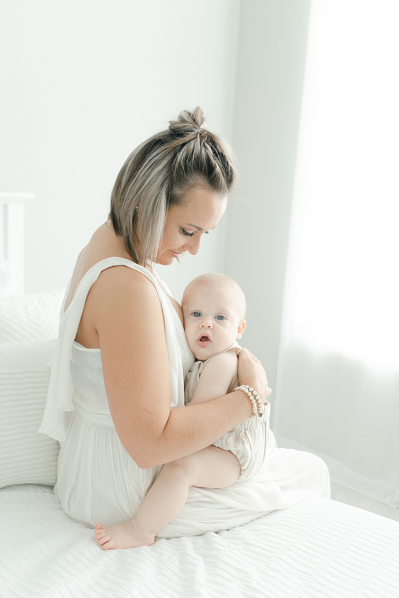 Mom sitting on a bed holding her baby boy | Photo by Little Sunshine Photography