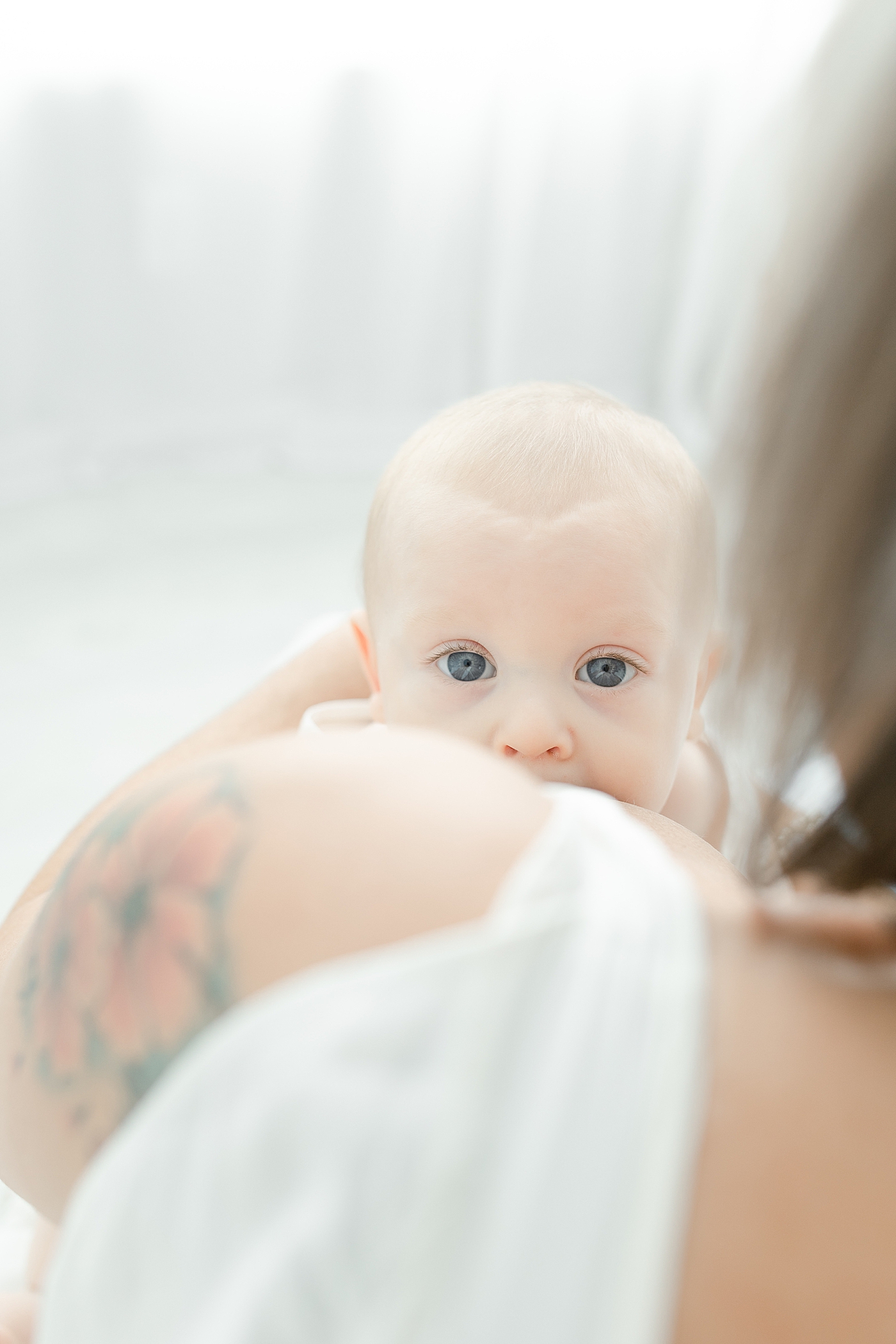 Baby boy looking over mom's shoulder while she breastfeeds | Photo by Little Sunshine Photography