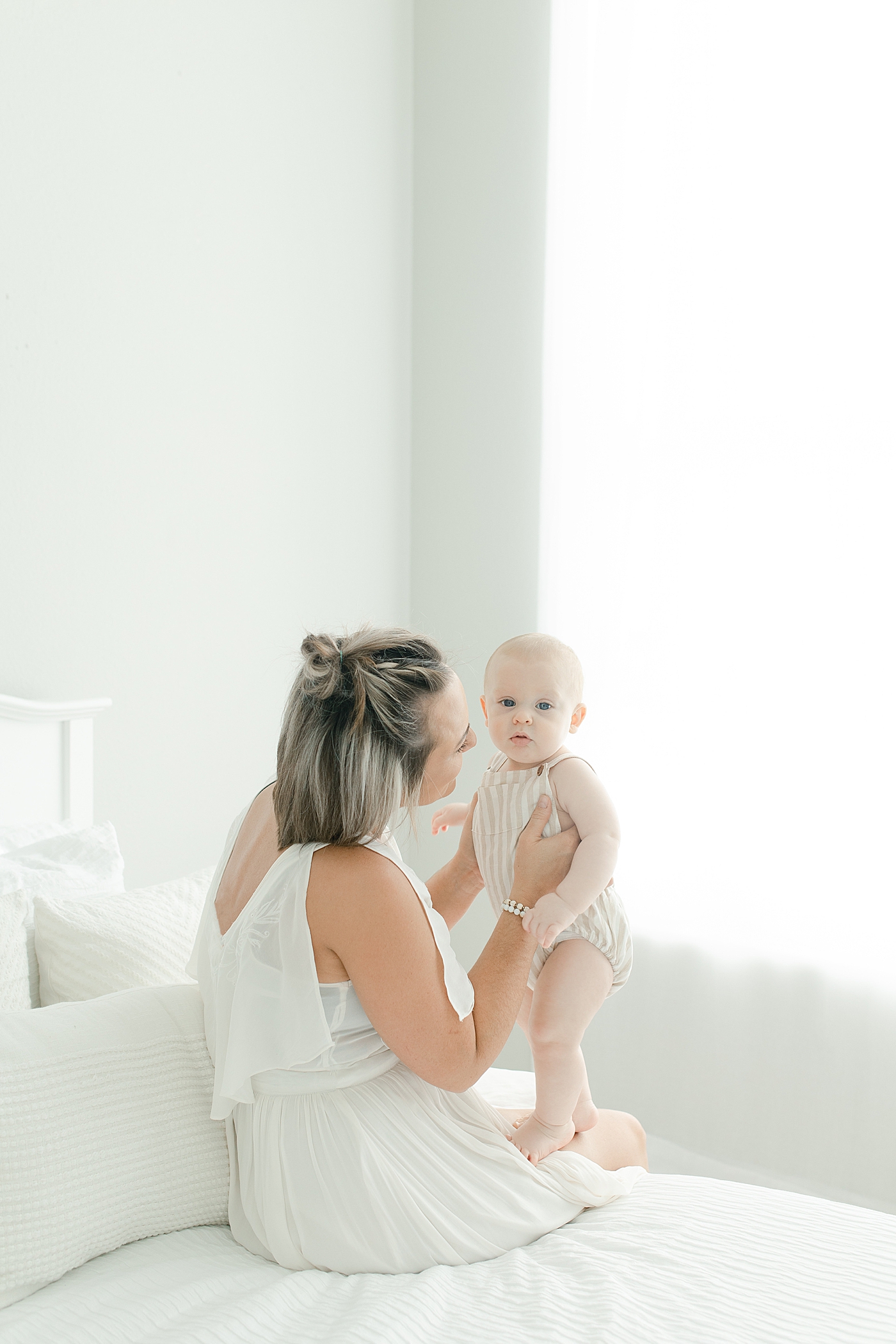 Mom sitting on a bed in white dress snuggling her baby boy | Photo by Hattiesburg Baby Photographer Little Sunshine Photography