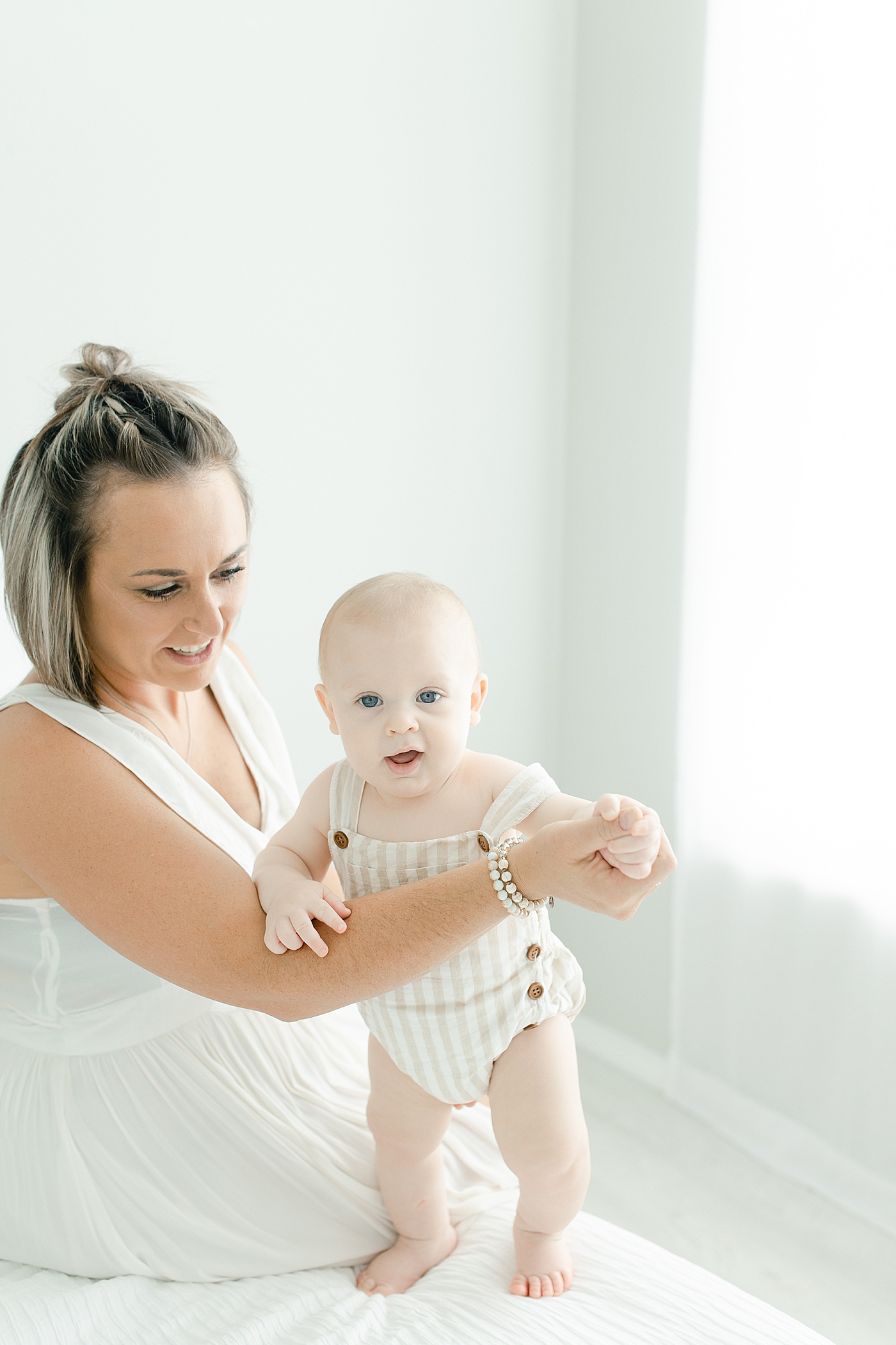 Mom helping her baby boy in striped pajamas stand | Photo by Hattiesburg Baby Photographer Little Sunshine Photography